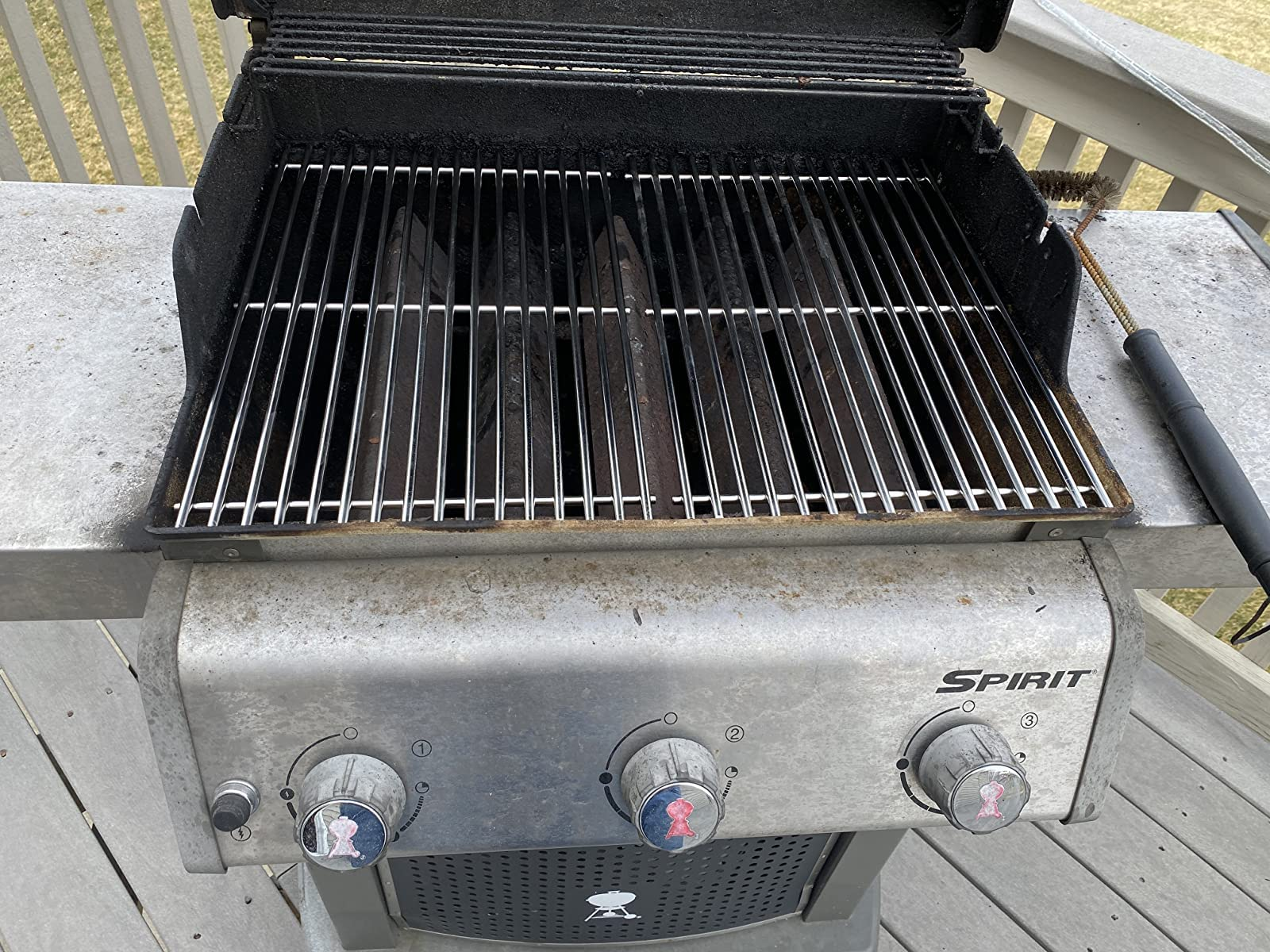 Ein offener, gebrauchter Spirit-Gasgrill mit Edelstahlrosten steht auf einer Holzterrasse.