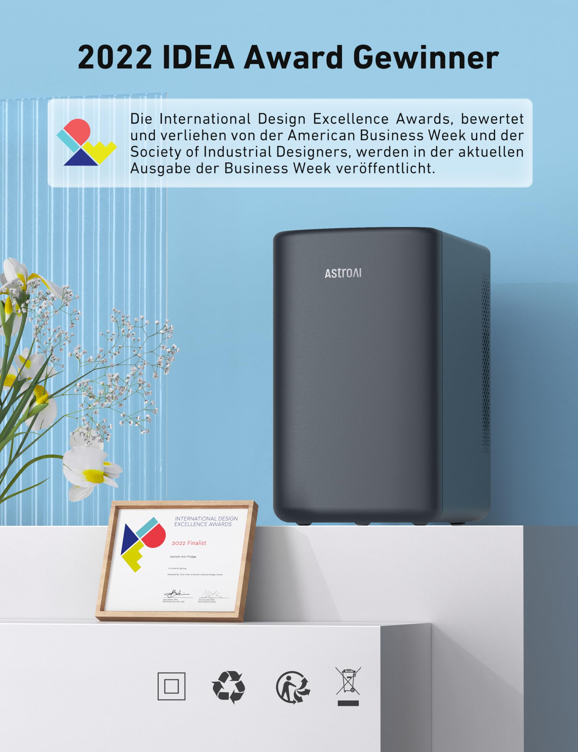 Ein grauer AstroAI Mini-Kühlschrank, eine Auszeichnung und Blumen stehen auf einer weißen Oberfläche vor blauem Hintergrund.