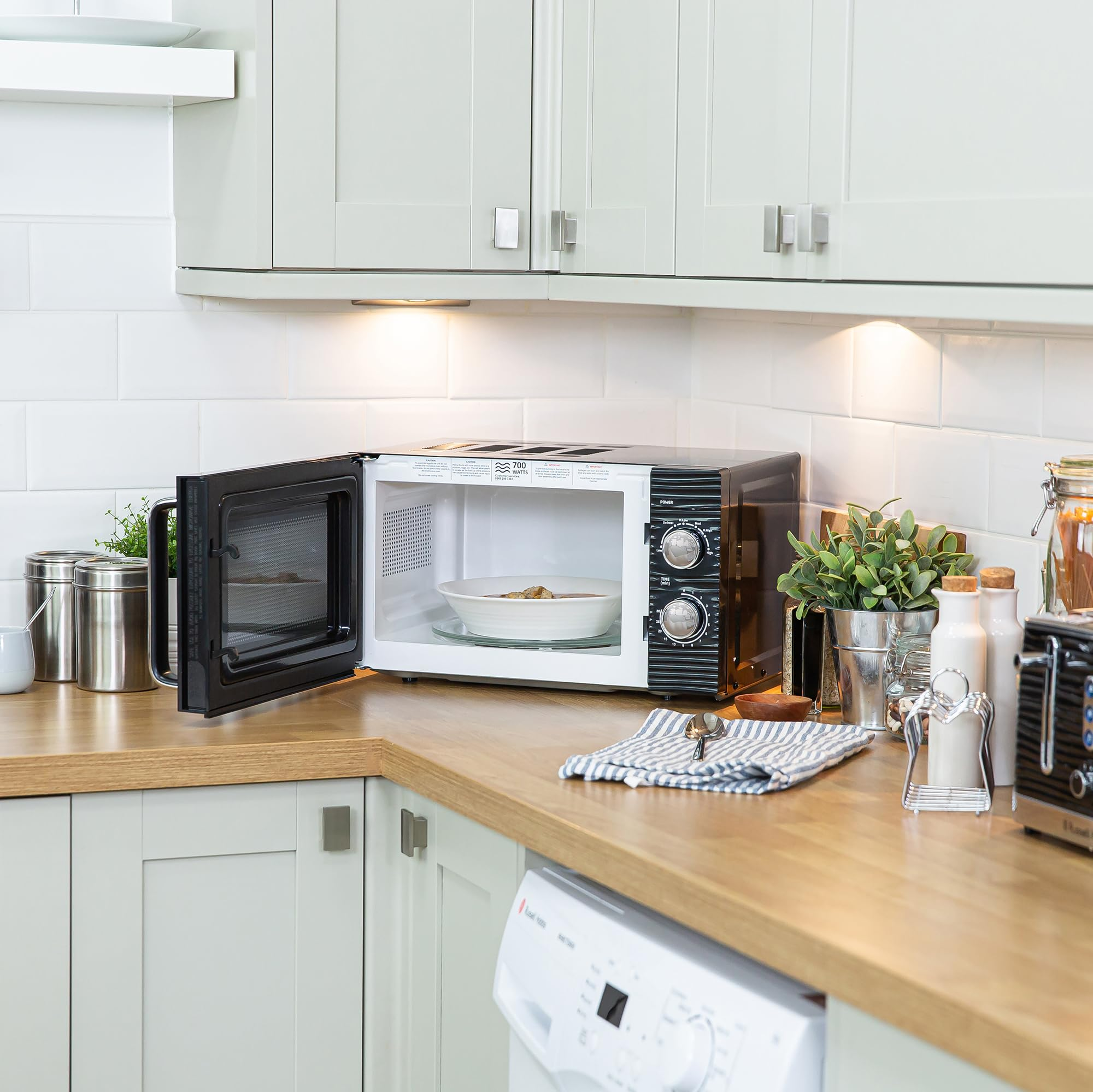 Un micro-ondes ouvert est posé sur un plan de travail en bois dans une cuisine lumineuse.