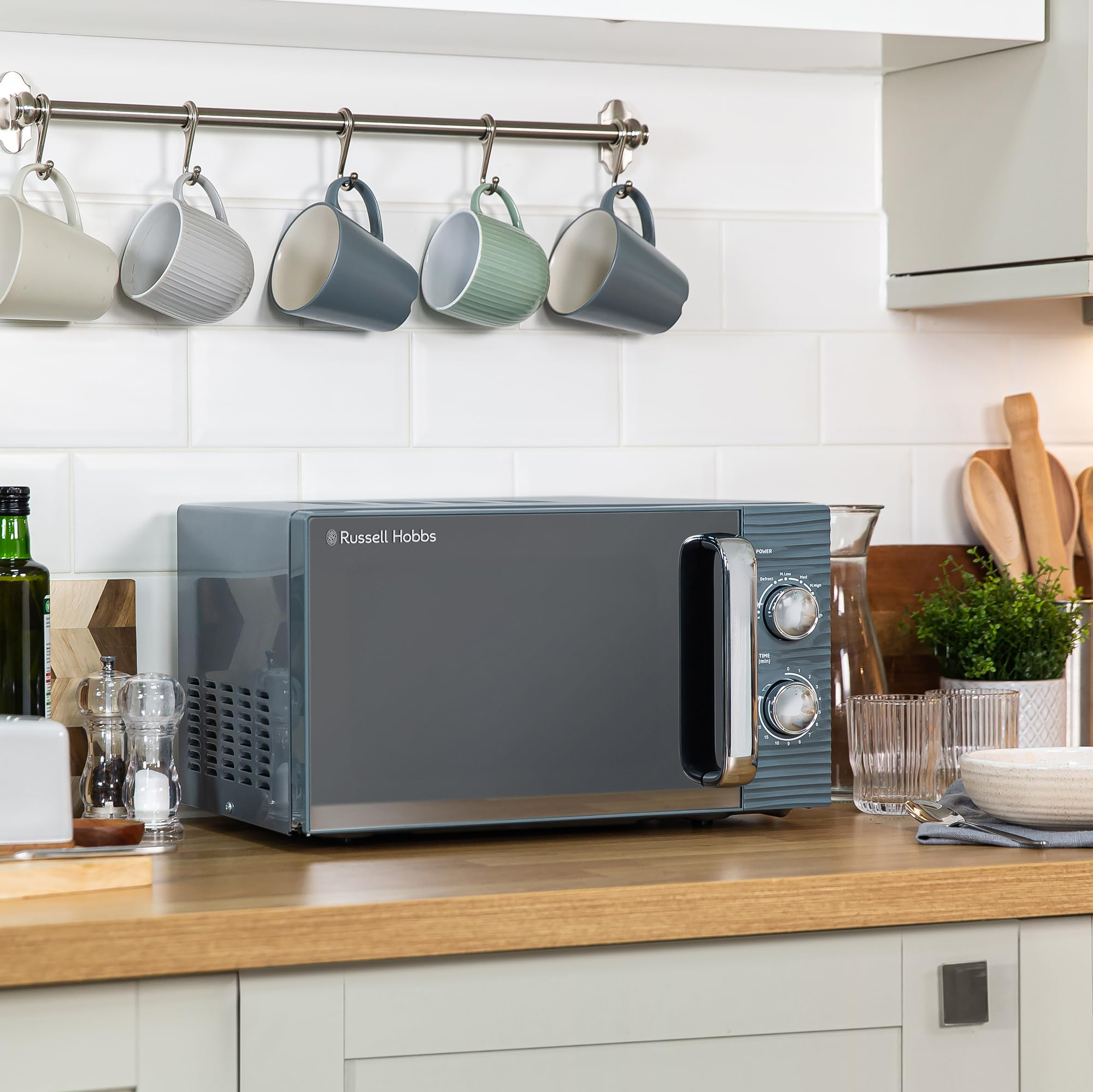 Un micro-ondes gris Russell Hobbs posé sur un plan de travail en bois dans une cuisine.