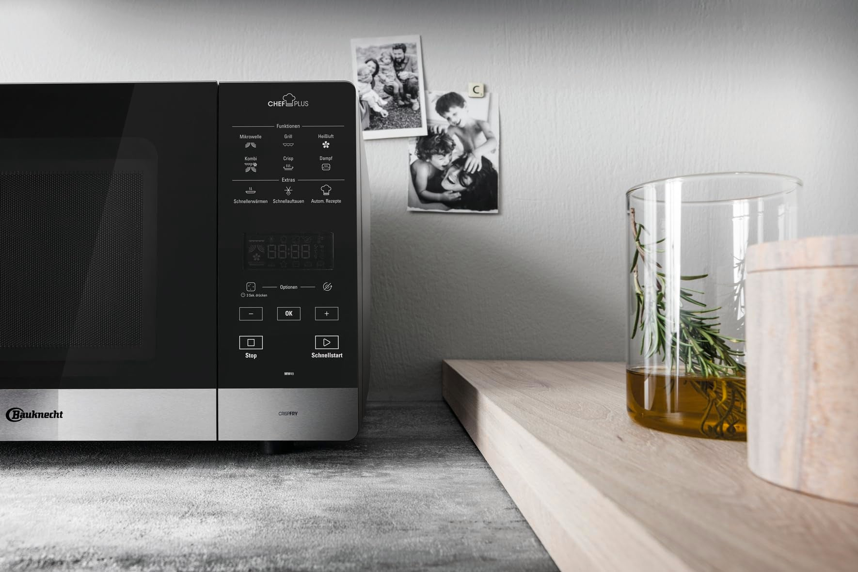Micro-ondes noir sur plan de travail gris à côté d'un verre d'herbes et de photos au mur.