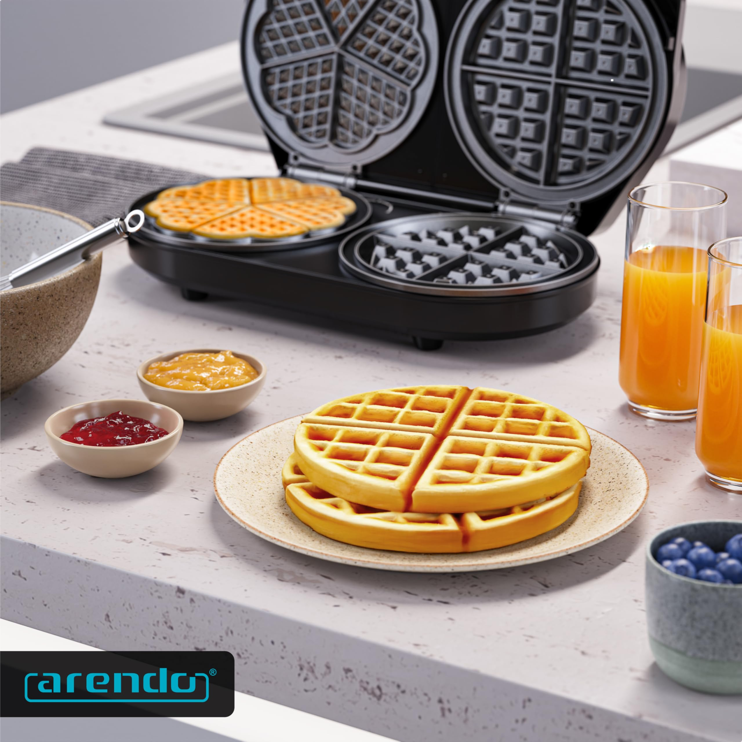 Ein offenes Waffeleisen auf einer Theke mit frischen Waffeln, Joghurt, Beeren und Gläsern mit Saft.