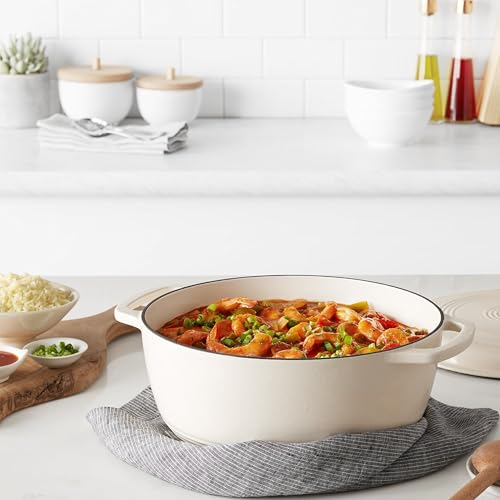 Une cocotte blanche remplie de crevettes et de légumes repose sur un torchon gris.