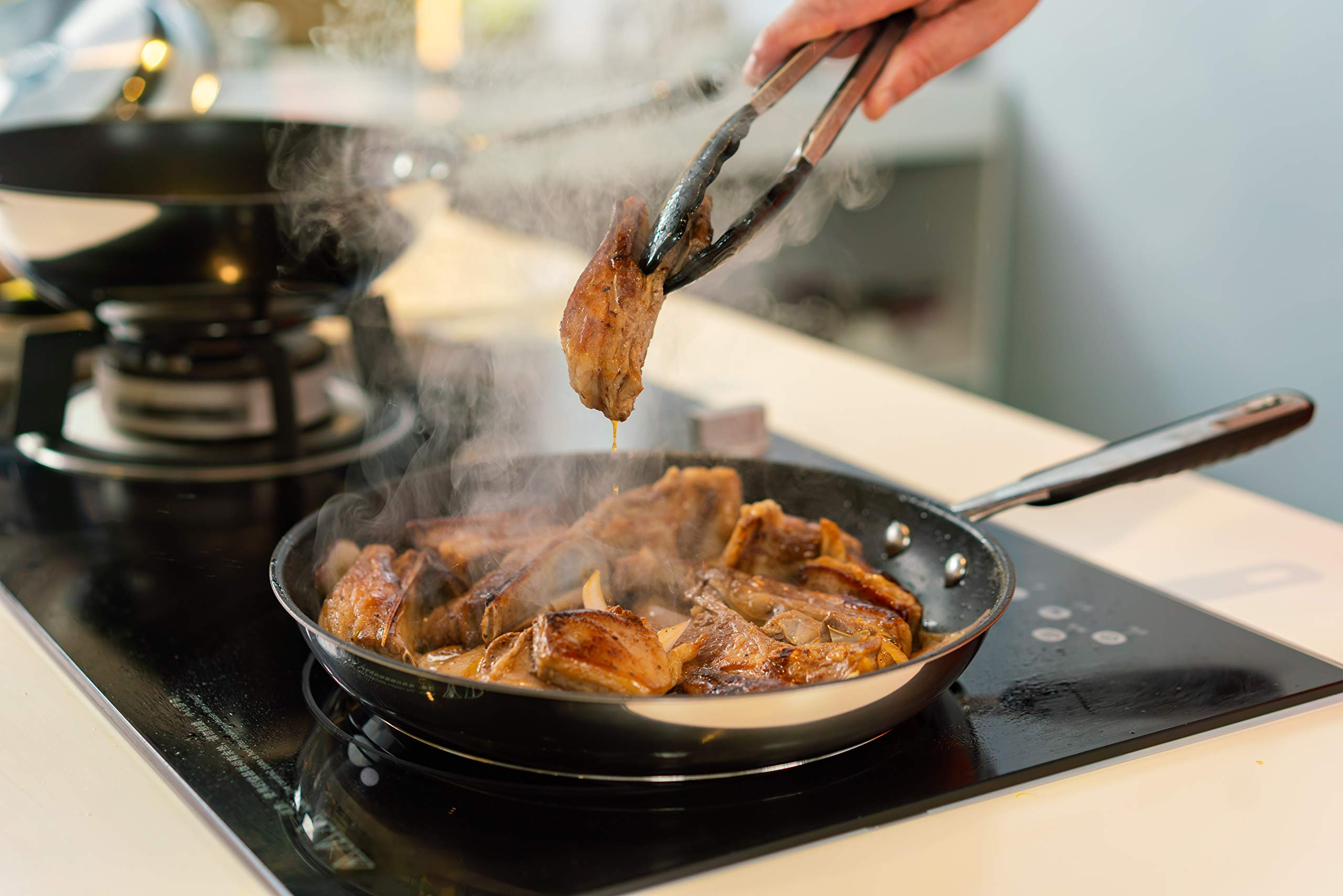 Des pinces soulevant un morceau de viande grésillant d'une poêle chaude avec des côtes.