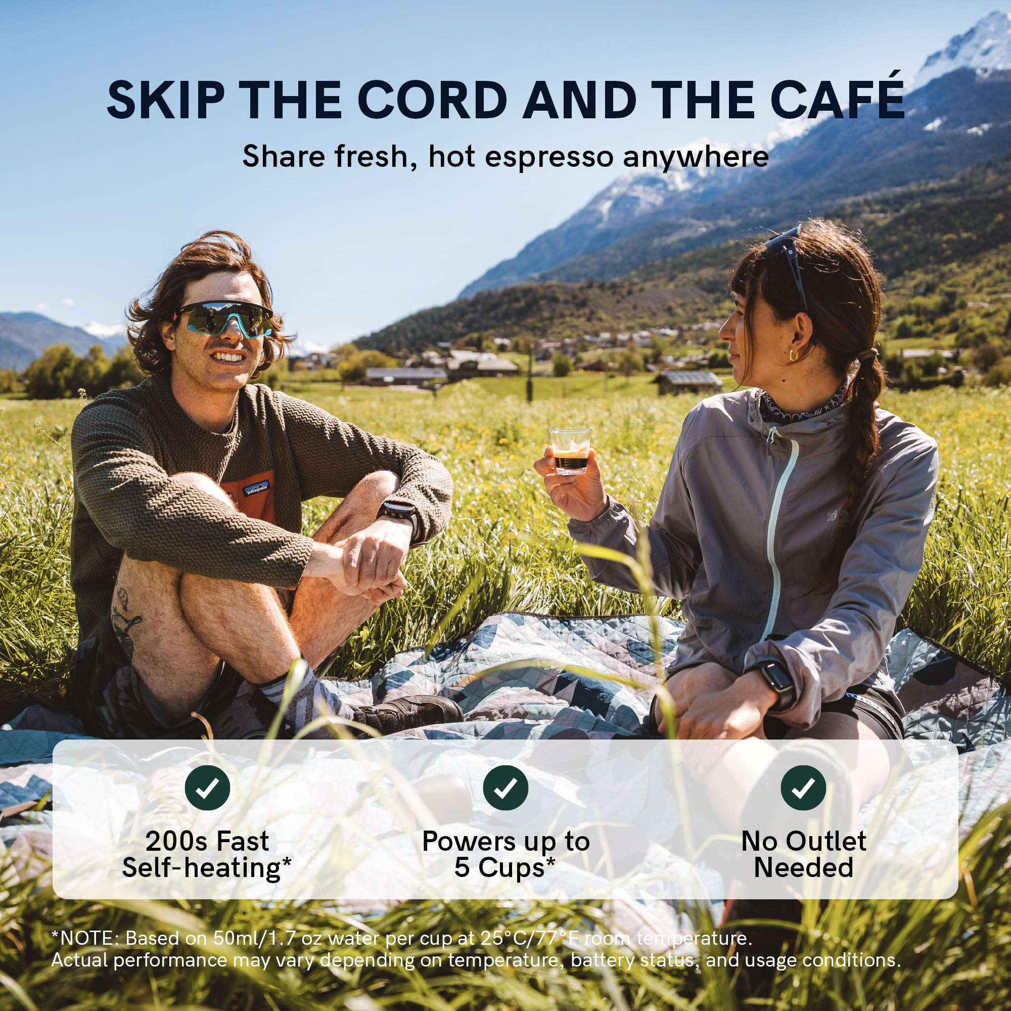 Un homme et une femme assis sur une couverture dans un champ, tenant des tasses d'espresso avec des montagnes.