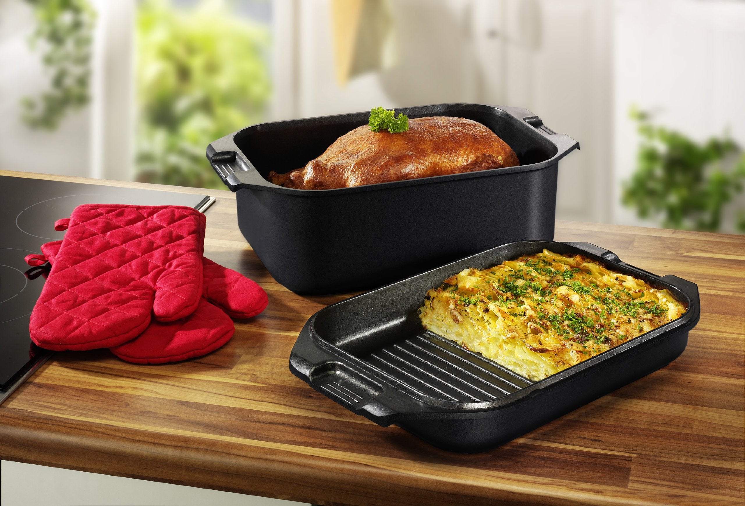 Un poulet rôti dans un plat noir et un gratin dans une poêle à gril sur un plan de travail en bois.