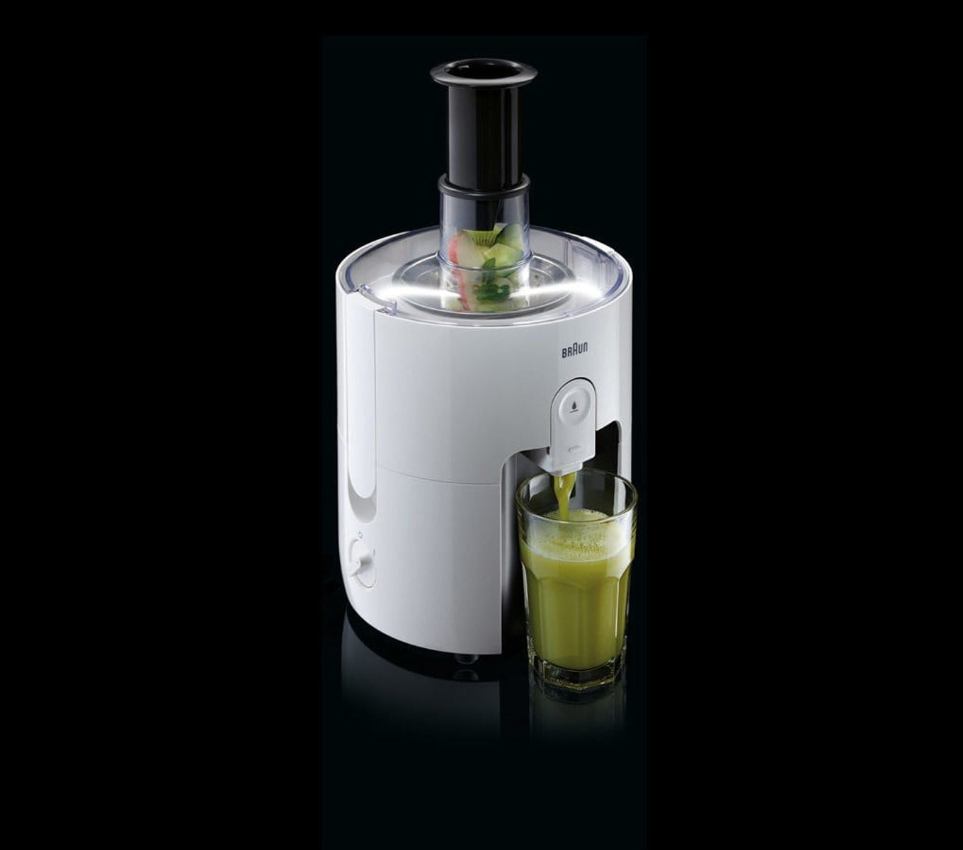 Una centrifuga bianca versa succo verde in un bicchiere su sfondo nero.