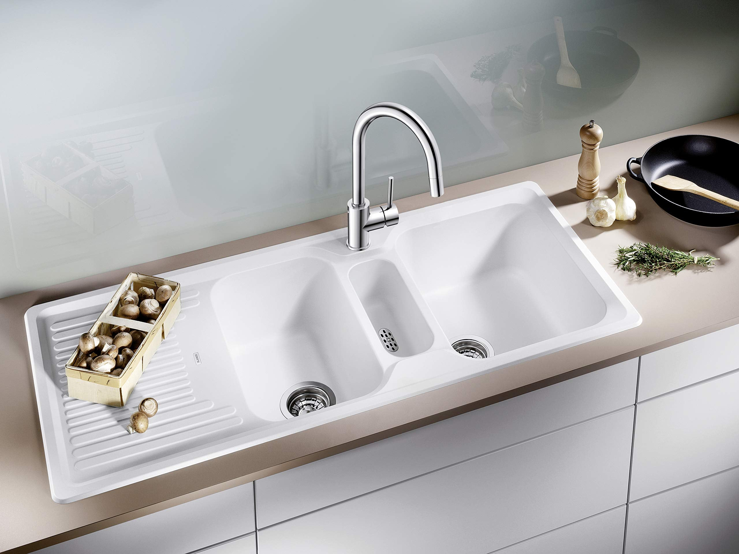 Ein weiße Küchenspüle mit Chromarmatur, Pilzen in einer Holzkiste und Küchenutensilien auf der Arbeitsplatte.
