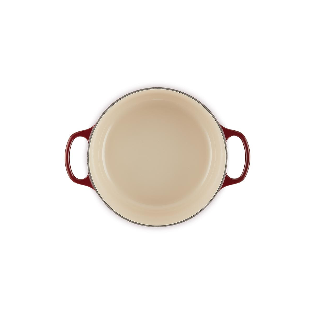 Une cocotte ronde en fonte rouge vue du dessus, avec un intérieur beige et deux poignées sur fond blanc.