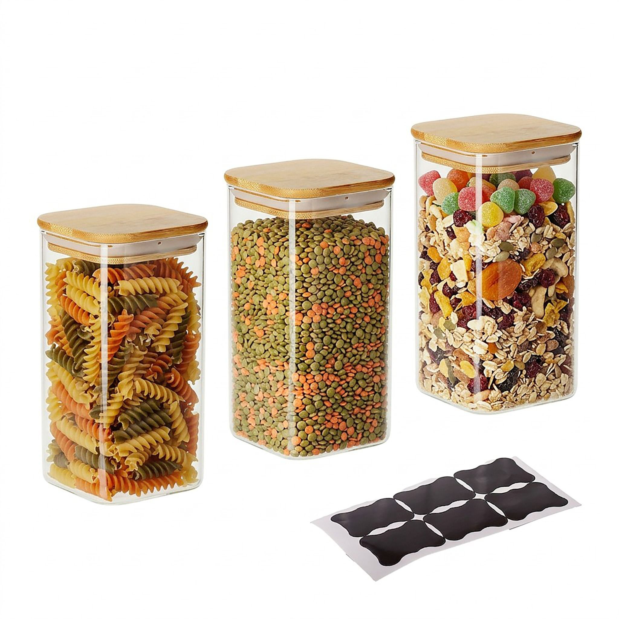 Drei Glasbehälter mit Bambusdeckel gefüllt mit Nudeln, Linsen und Müsli, daneben schwarze Etiketten.