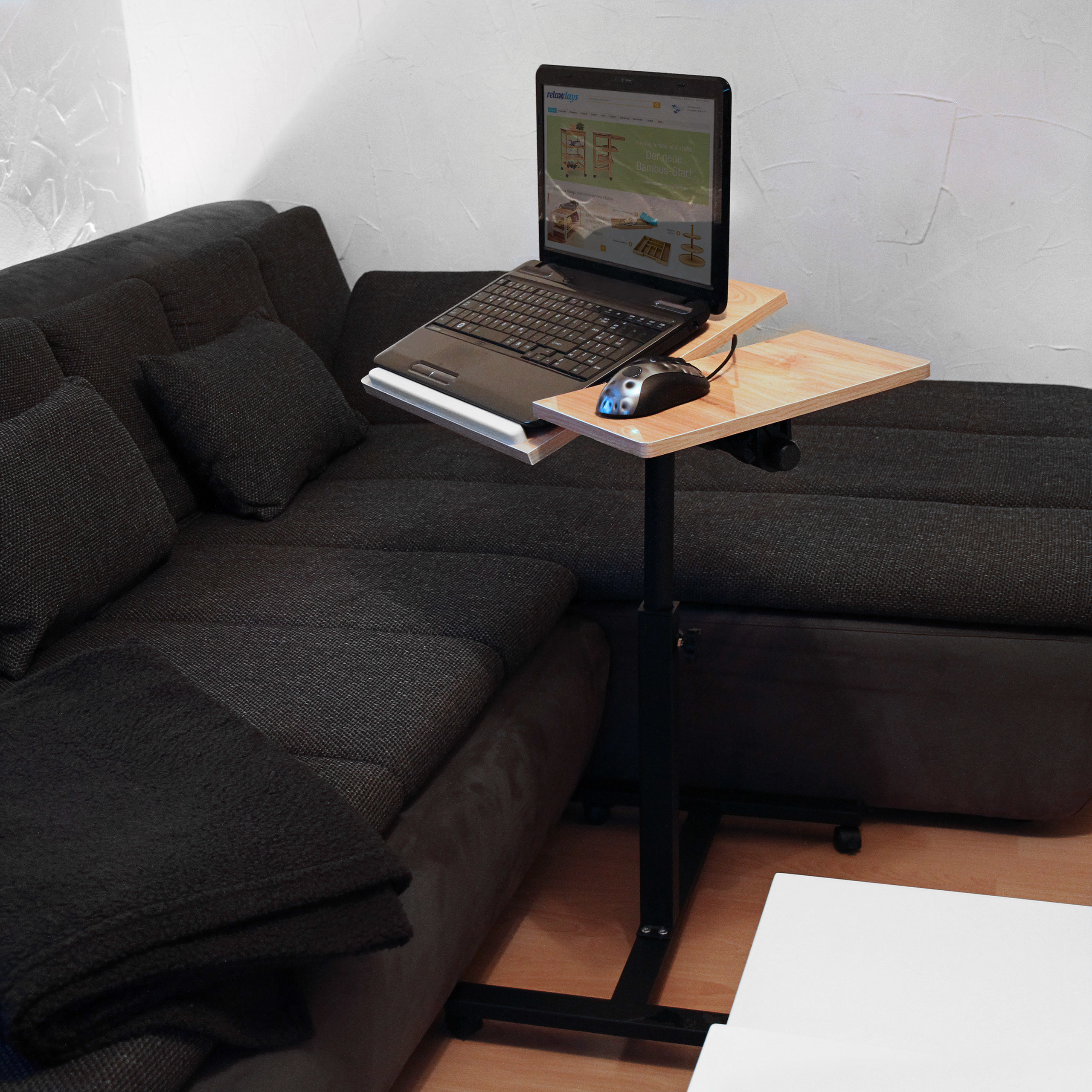 Ein Laptop steht auf einem kleinen verstellbaren Holztisch neben einem dunkelgrauen Ecksofa.