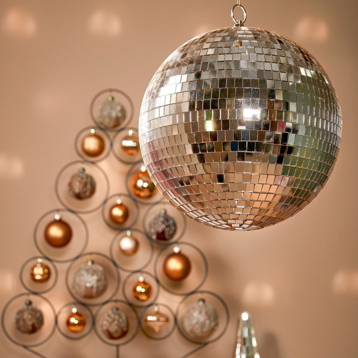 A hanging disco ball in the foreground, with a Christmas tree made of metal rings and ornaments behind it.