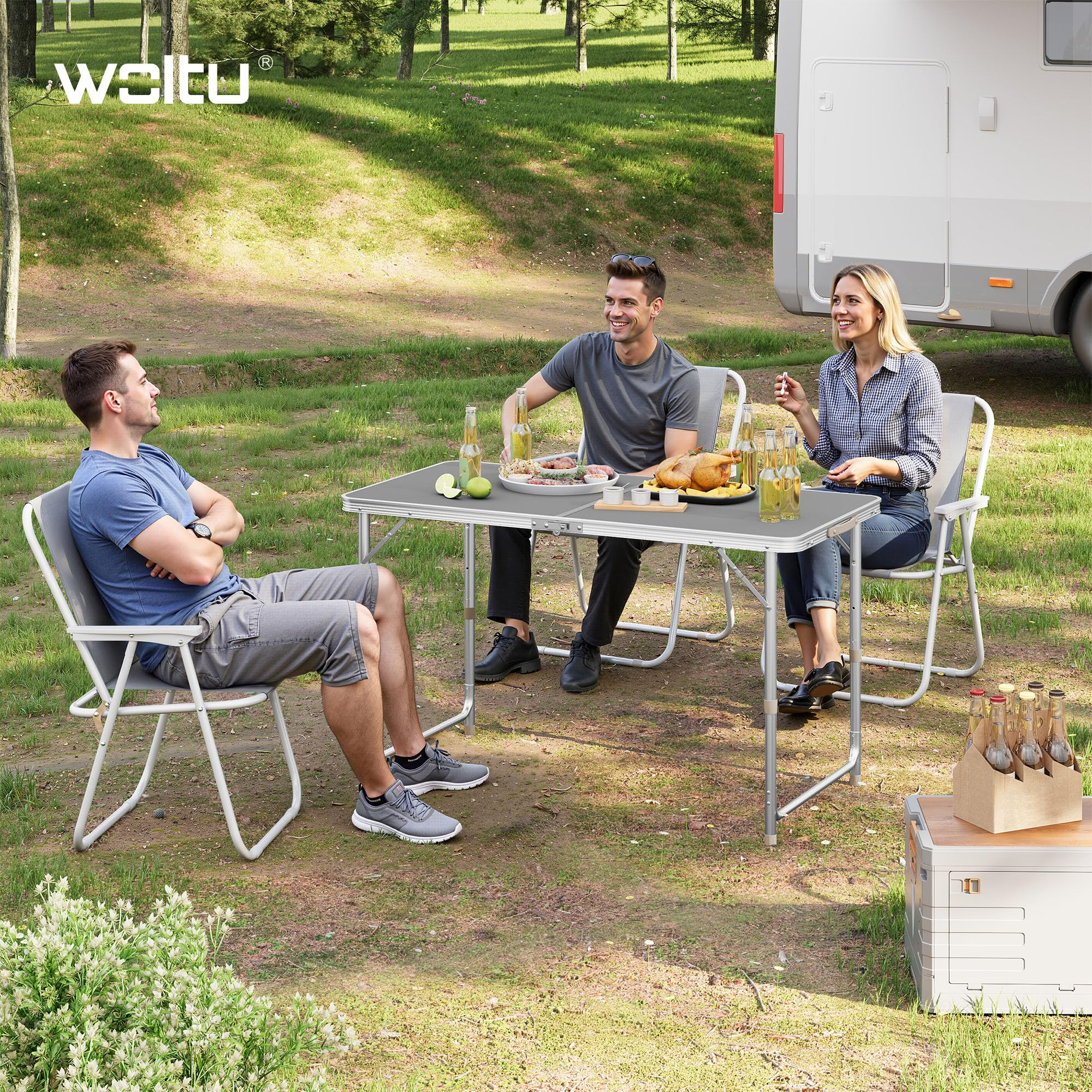 Tre persone siedono a un tavolo pieghevole all'aperto davanti a un camper, mangiando insieme.
