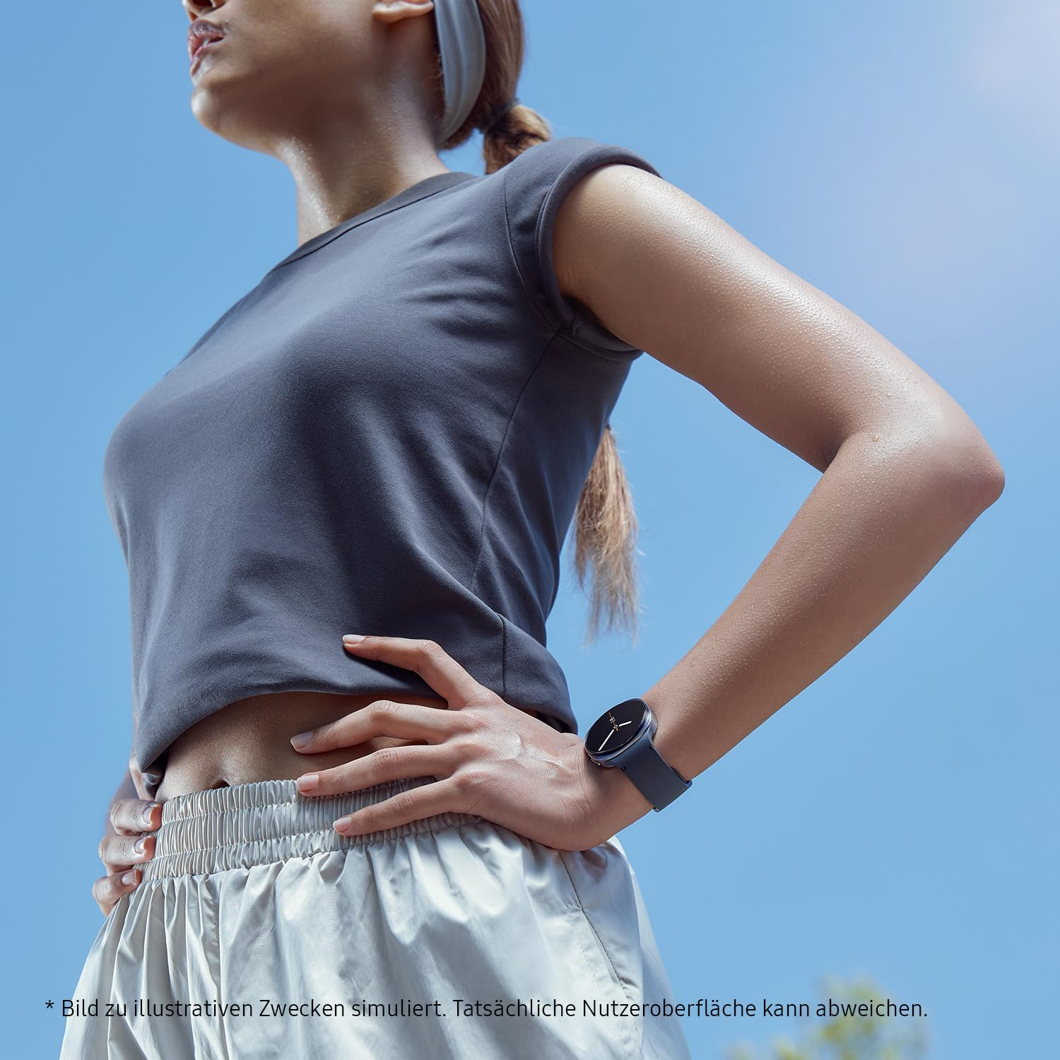 Une athlète en haut gris et short porte une montre connectée au poignet sous un ciel bleu.