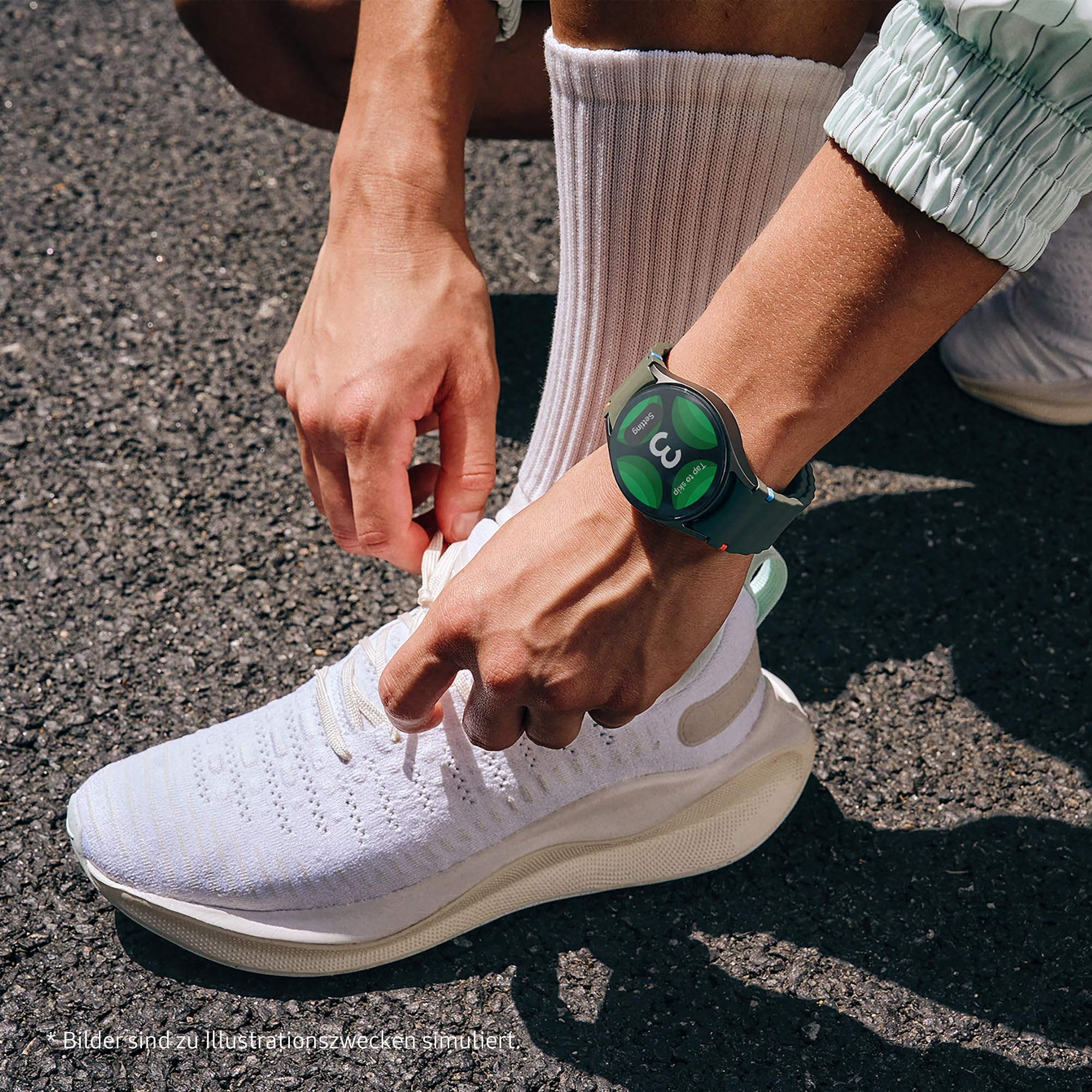 Persona che allaccia scarpe da ginnastica bianche, indossando uno smartwatch verde al polso su asfalto.