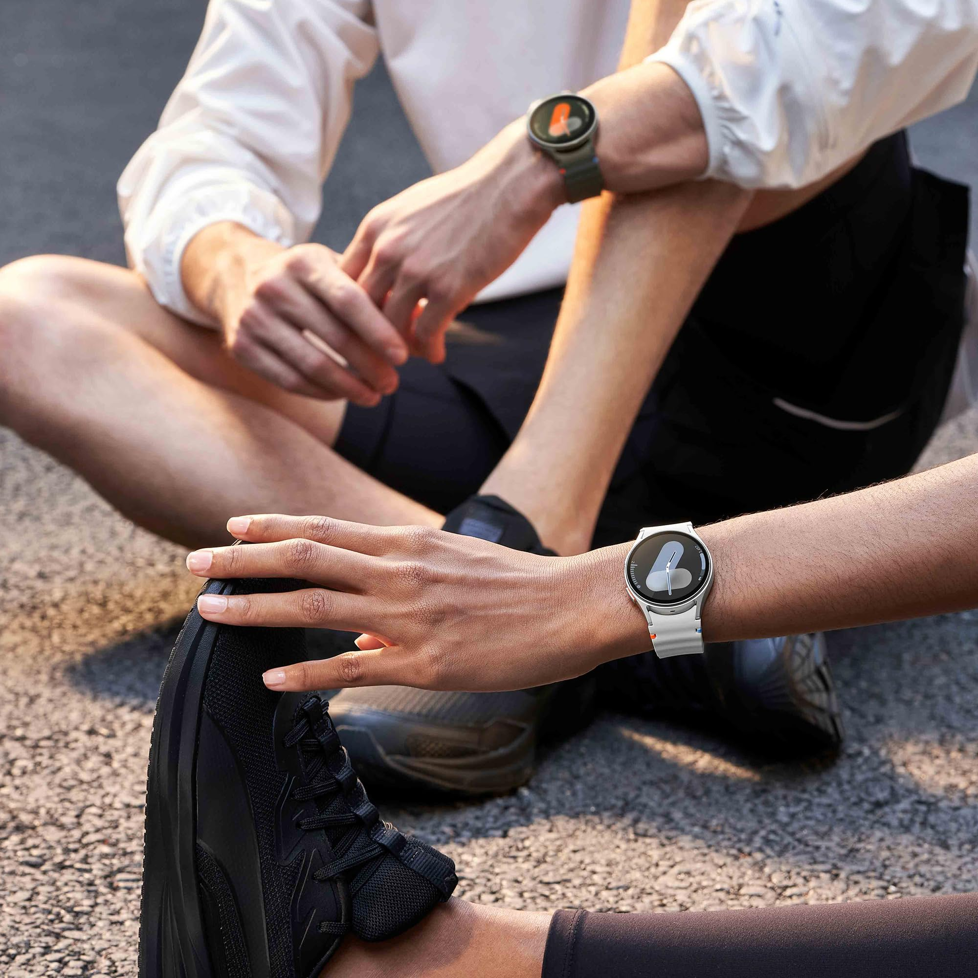 Due corridori seduti all'aperto, con abbigliamento sportivo e smartwatch, uno che si allunga.
