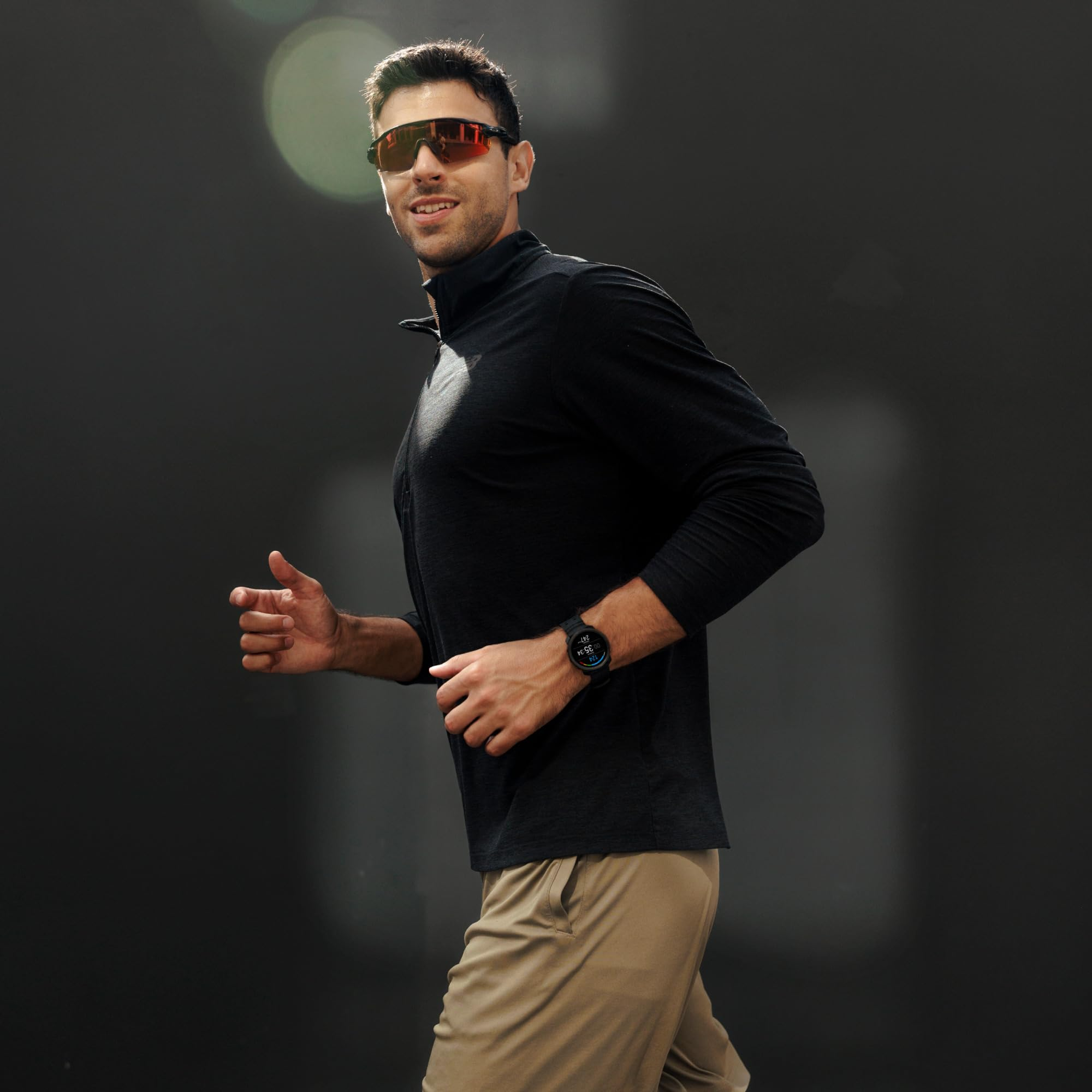 Un uomo con camicia nera a maniche lunghe e pantaloncini beige corre su sfondo scuro.