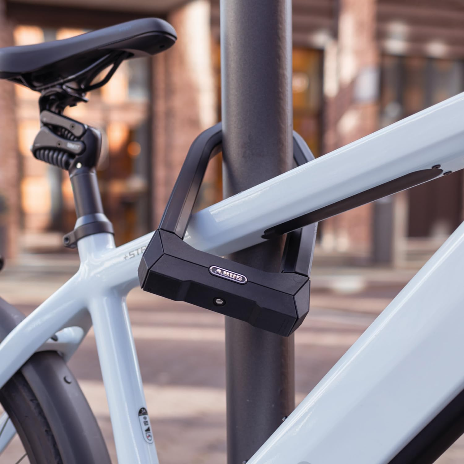 Un vélo bleu clair attaché à un poteau avec un antivol en U noir, sur un fond urbain flou.