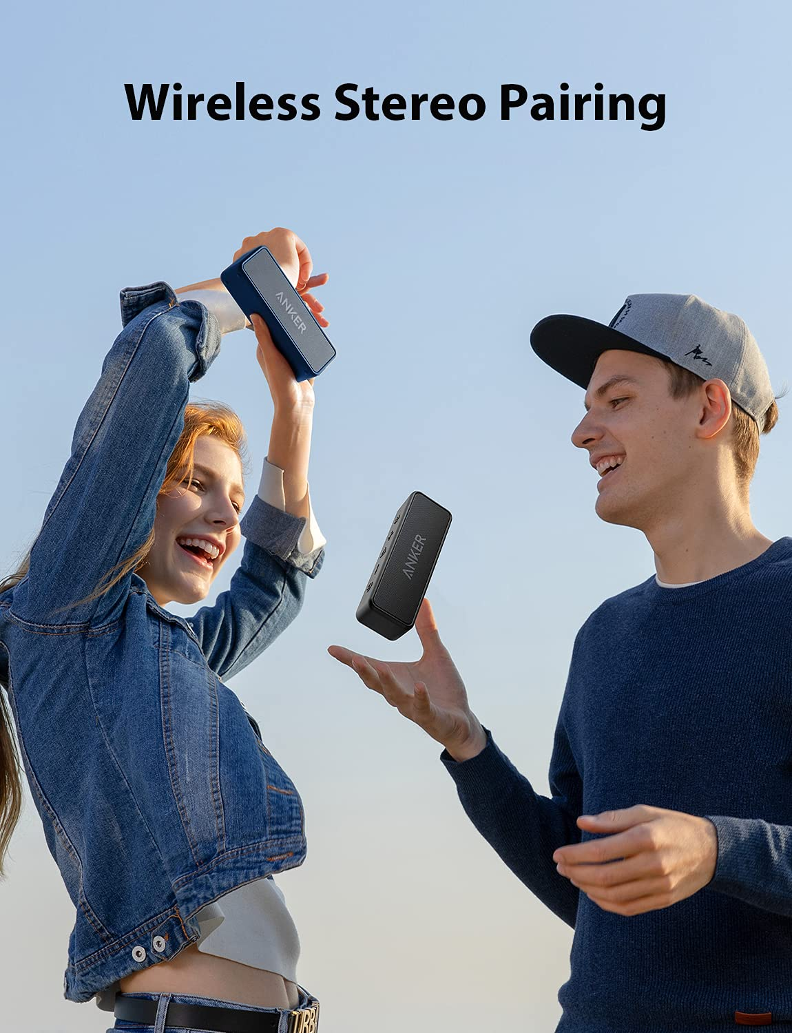 Deux jeunes sourient et tiennent des haut-parleurs sans fil Anker sous un ciel bleu.