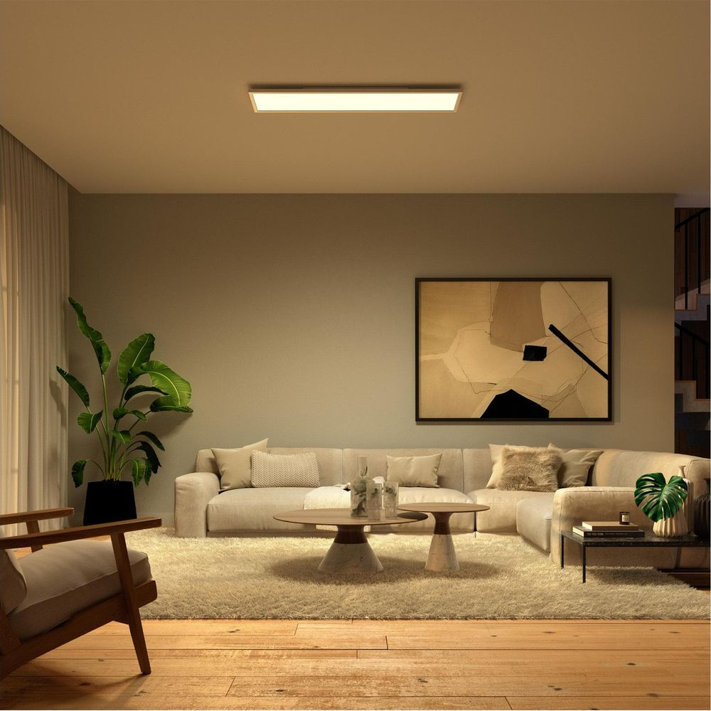 Soggiorno caldo e moderno con divano angolare beige, grande dipinto astratto e lampada da soffitto rettangolare.