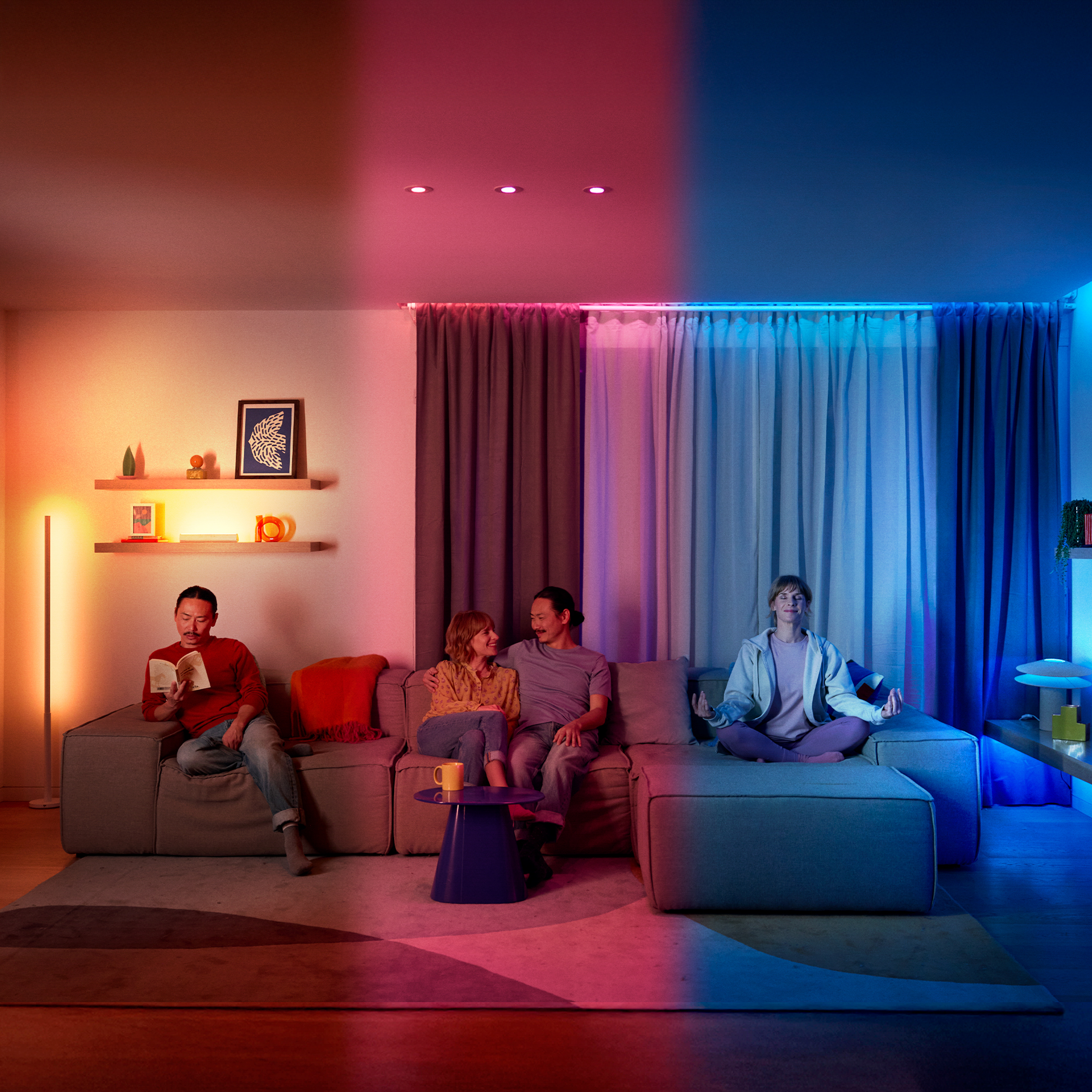 Soggiorno con illuminazione colorata, tre persone sul divano che leggono, parlano e meditano.