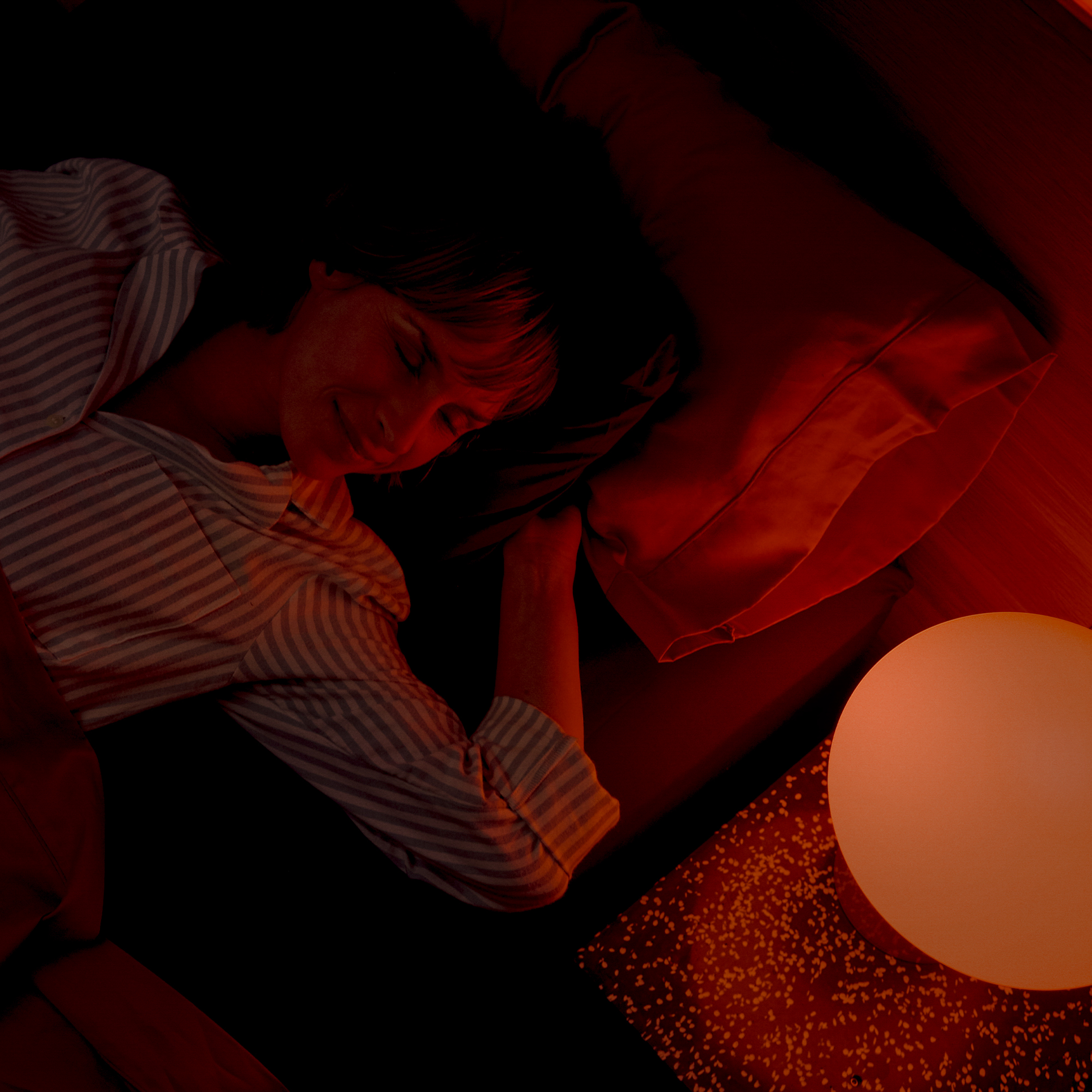 Una persona che dorme in un letto illuminato da luce rossa.