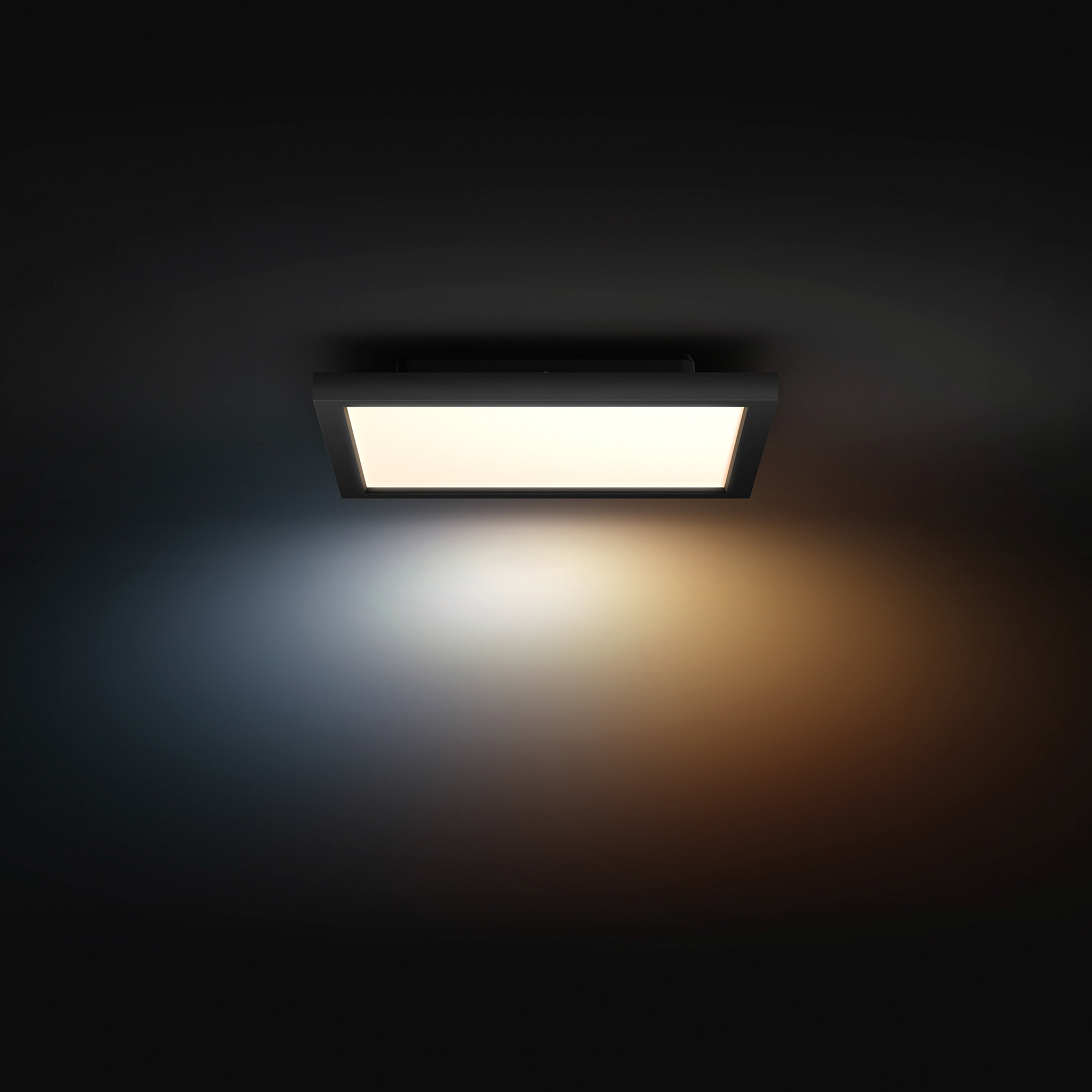 Una plafoniera nera quadrata si illumina, proiettando luce calda e fredda su una parete scura.