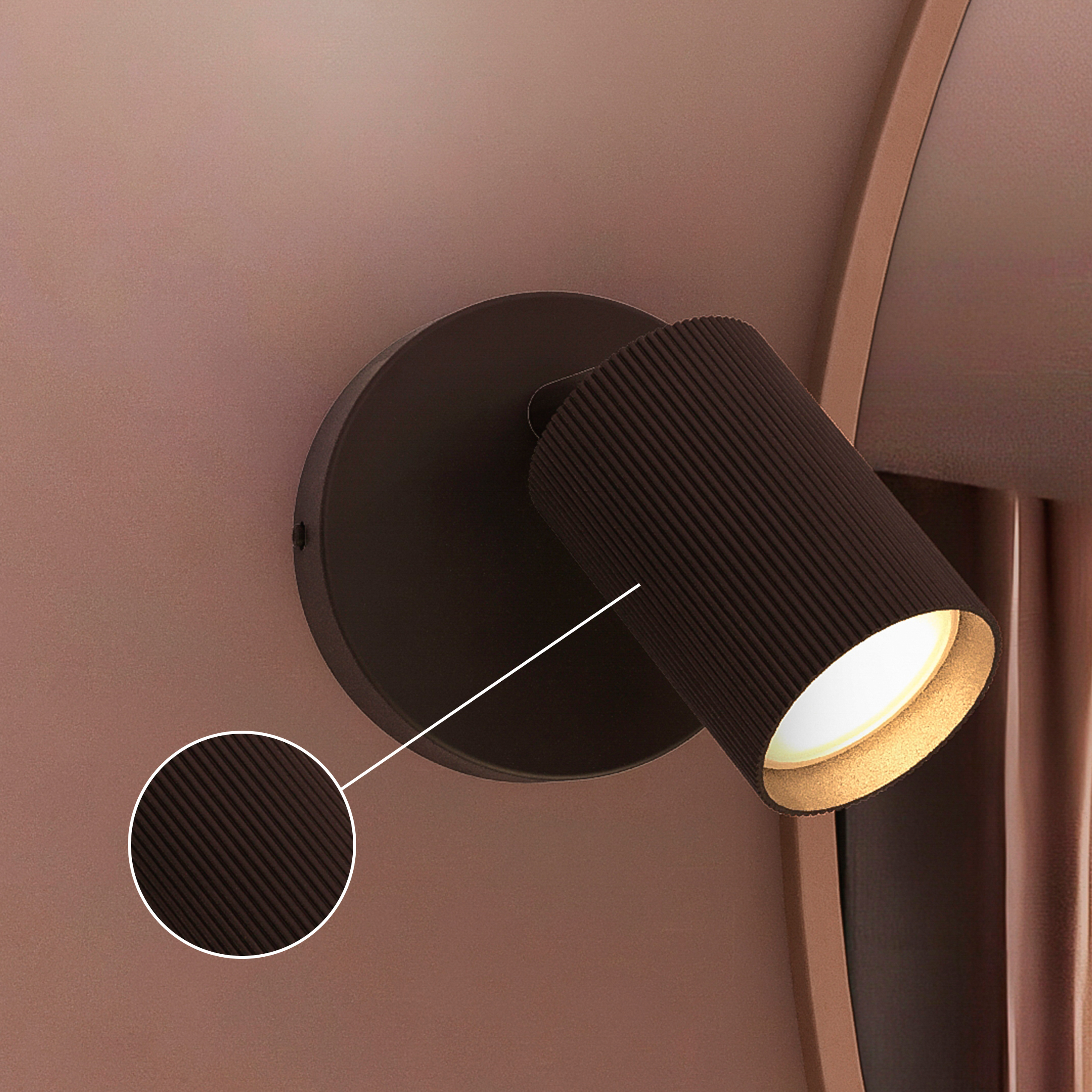 Eine schwarze, geriffelte Wandlampe leuchtet an einer rosa Wand mit runden Spiegel.