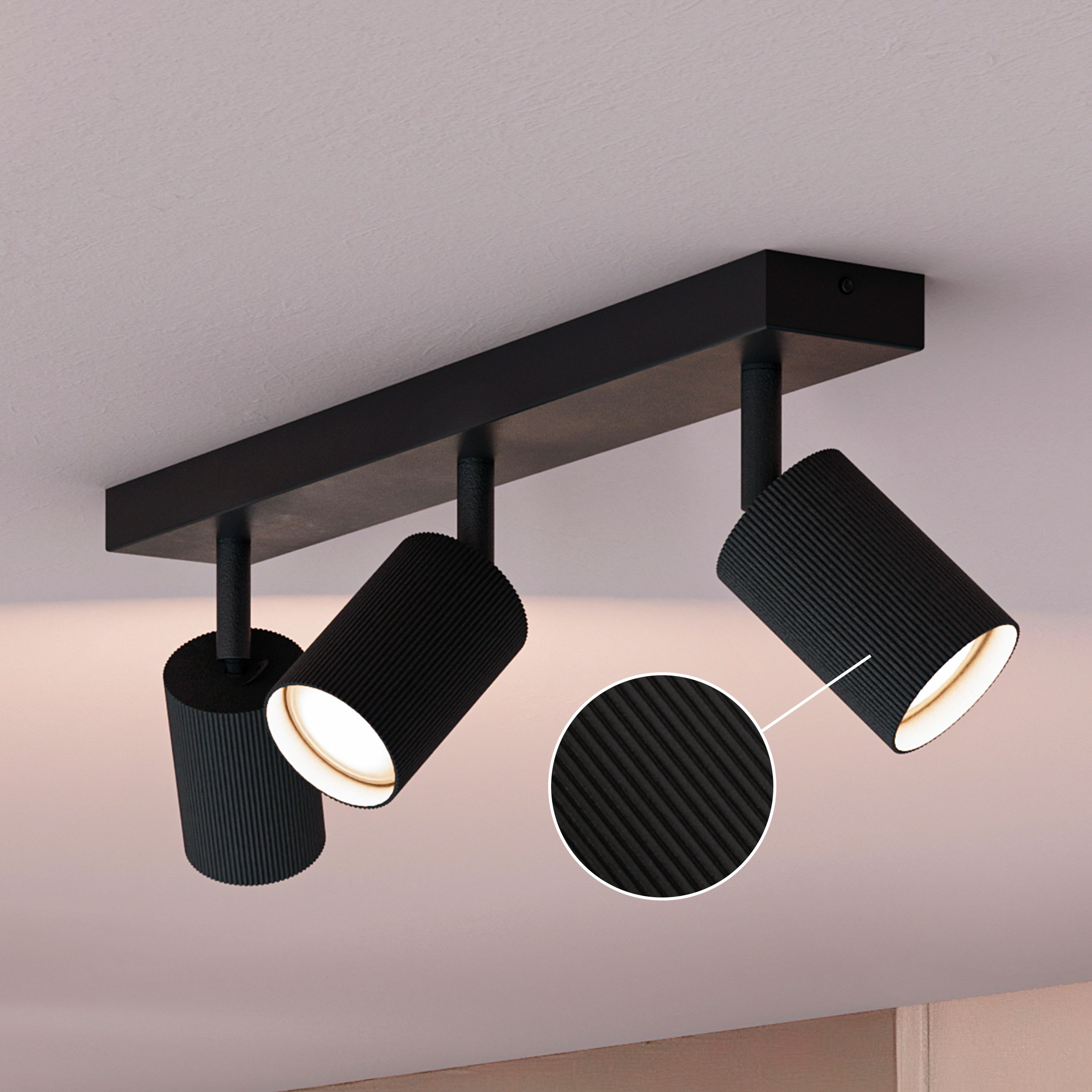 Schwarze Deckenleuchte mit drei gerippten Spots und Detailansicht auf weißer Decke.