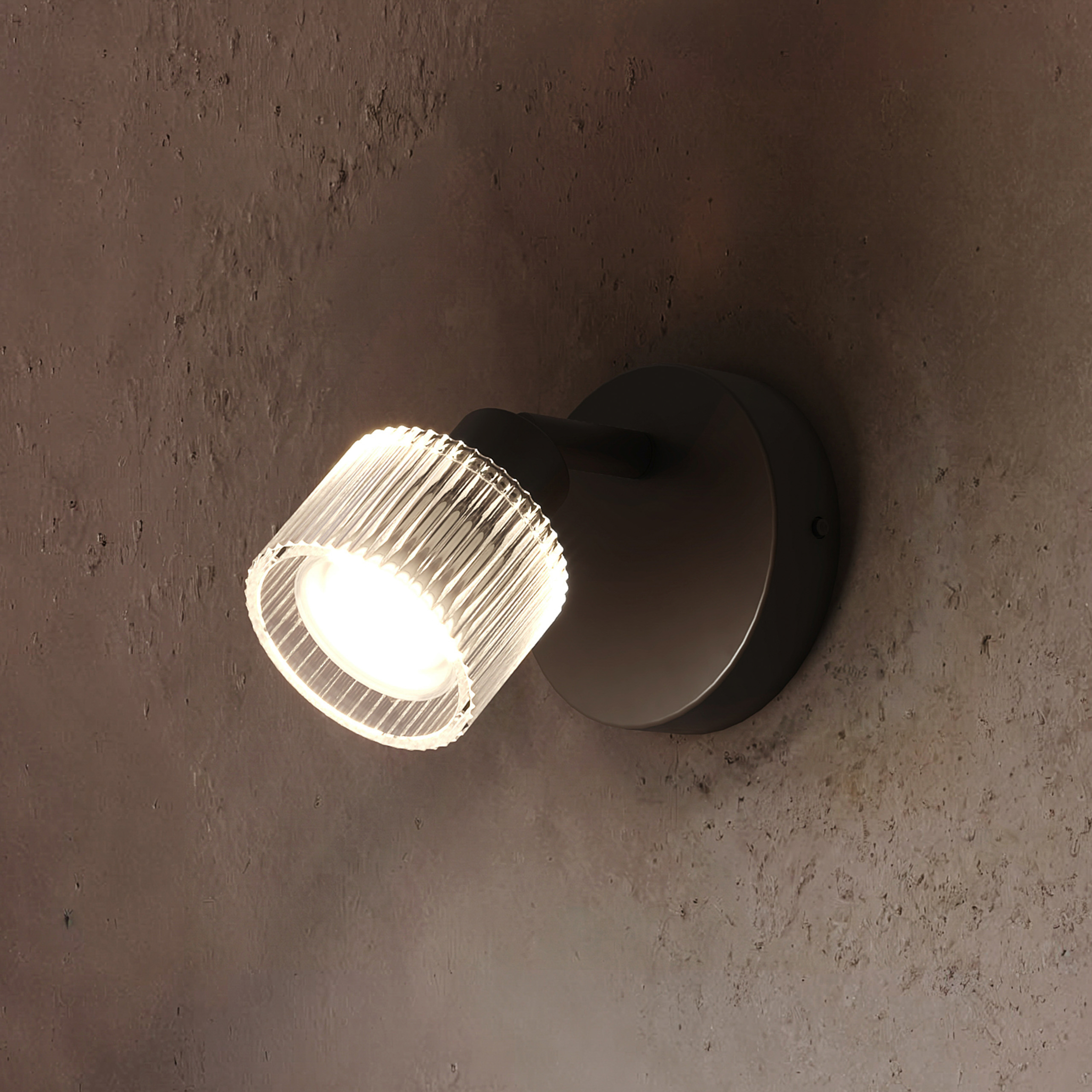 Eine moderne schwarze Wandleuchte mit leuchtendem, geriffeltem Glasschirm an einer strukturierten braunen Wand.