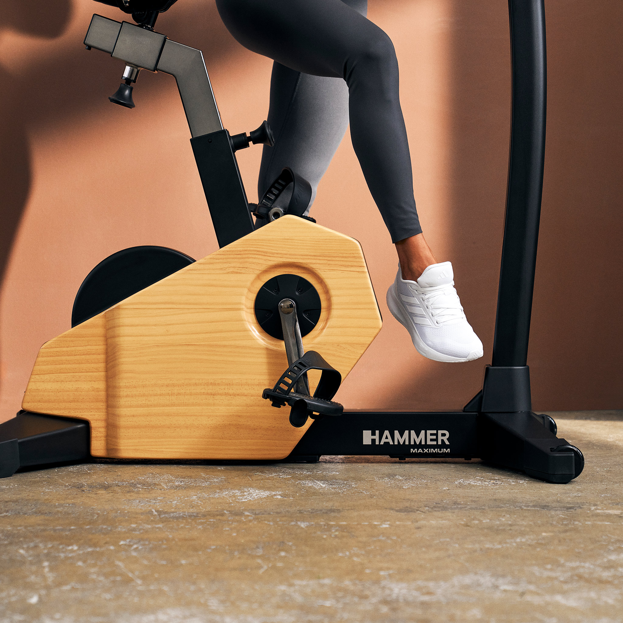 Person in grauen Leggings und weißen Sneakers trainiert auf einem Hammer Maximum Ergometer mit Holzoptik.