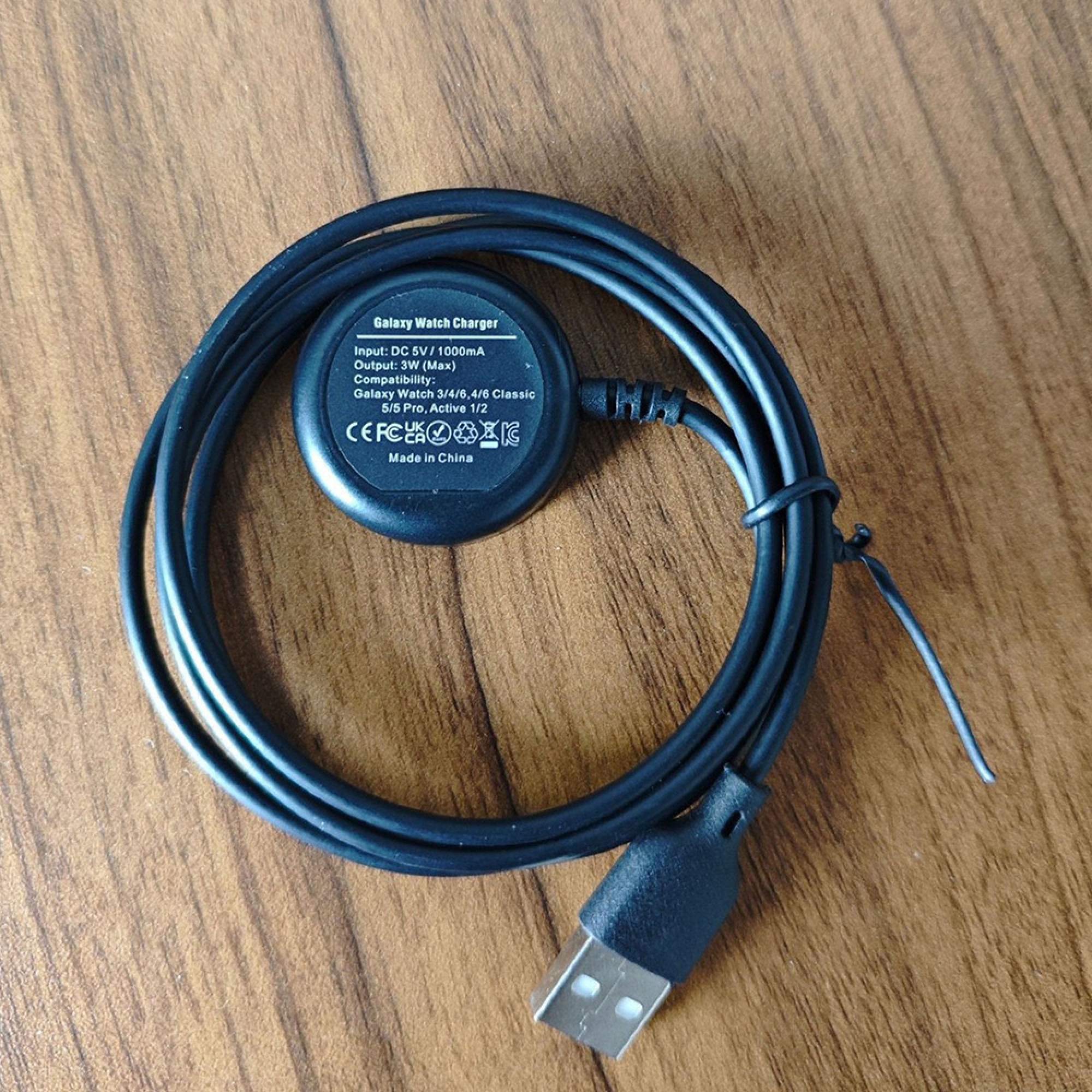 Ein schwarzes Galaxy Watch Ladekabel mit USB-Anschluss liegt auf einer Holzoberfläche.