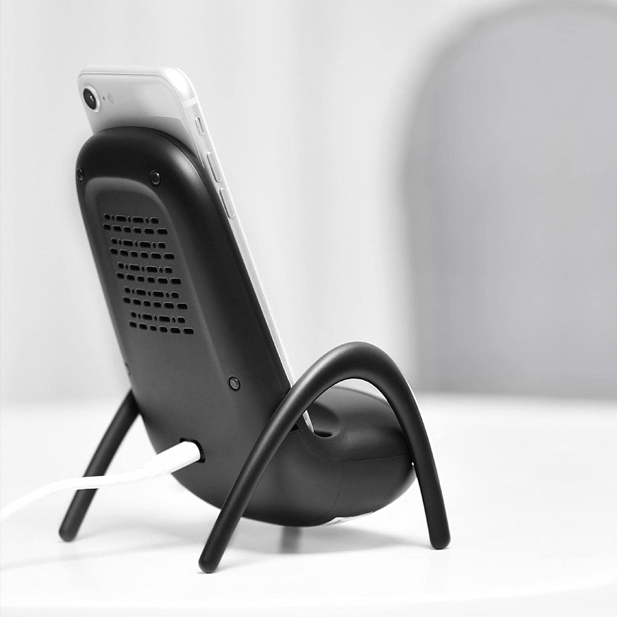 Ein Smartphone in einer schwarzen, insektenartigen kabellosen Ladestation mit geschwungenen Beinen und weißem Kabel.