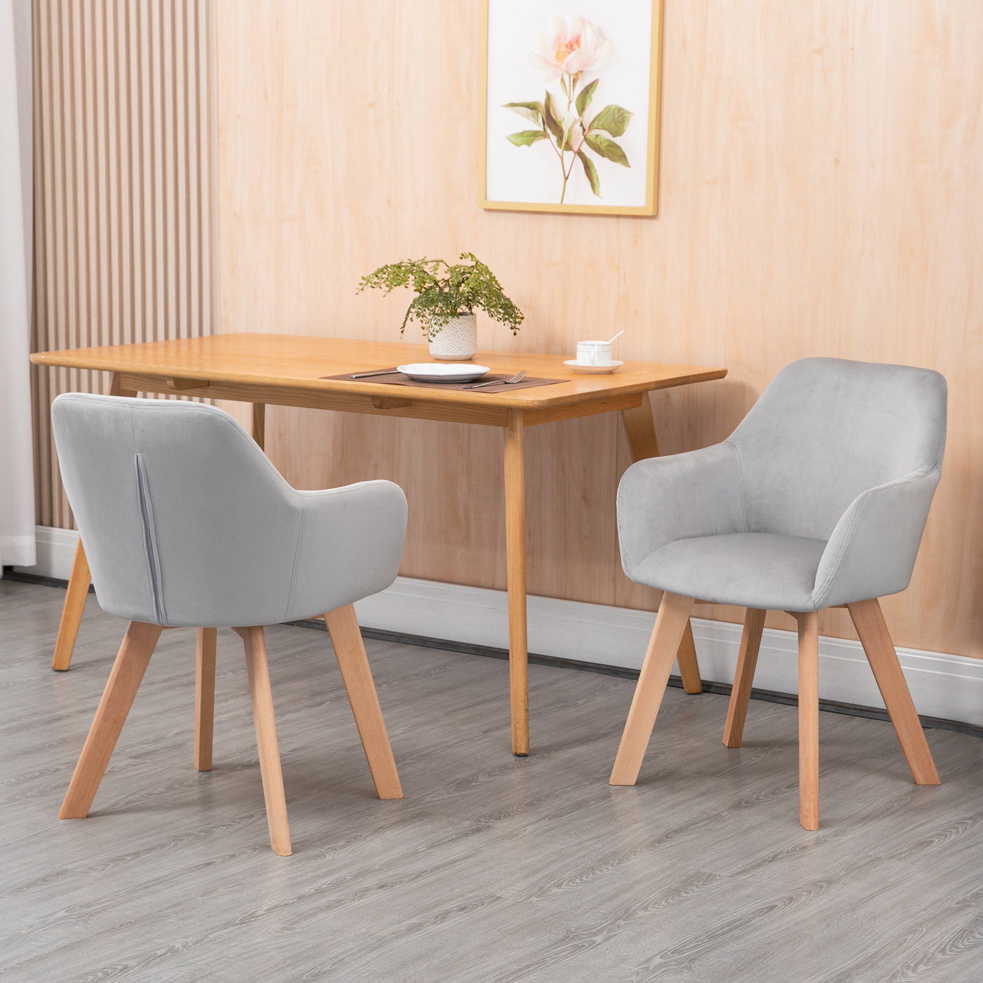 Due sedie grigie con gambe in legno a un tavolo in legno con parete boiserie.