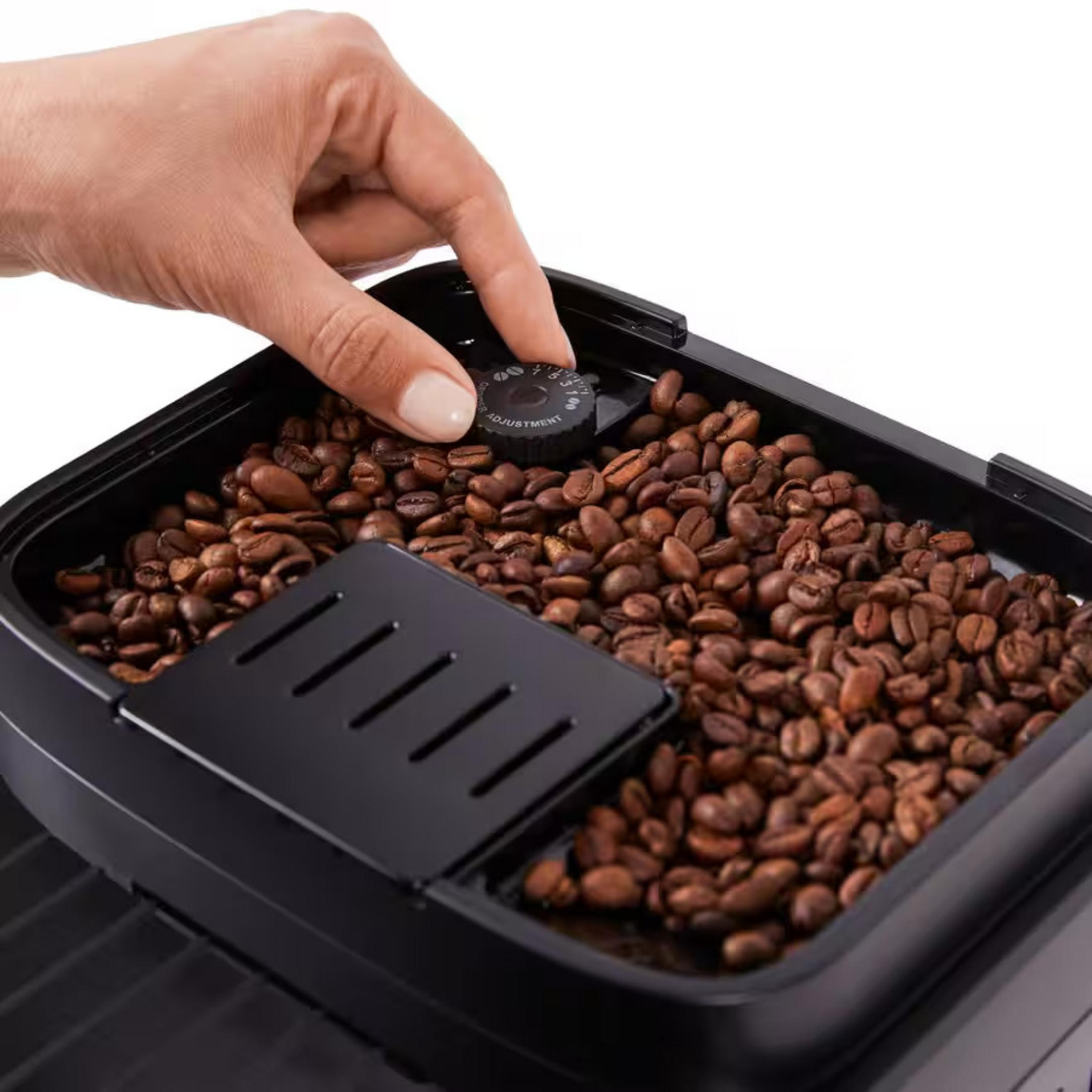 Una mano gira la manopola di macinatura in un contenitore di chicchi di caffè.
