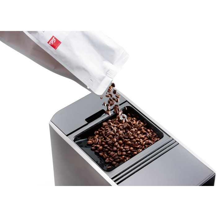 I chicchi di caffè vengono versati da un sacchetto bianco nella tramoggia di una macchina.