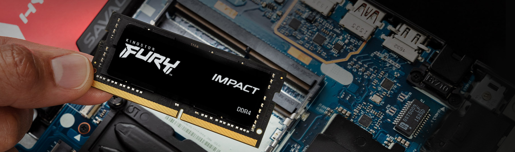 Hand hält einen schwarzen Kingston FURY Impact DDR4 RAM-Stick über ein blaues Motherboard.