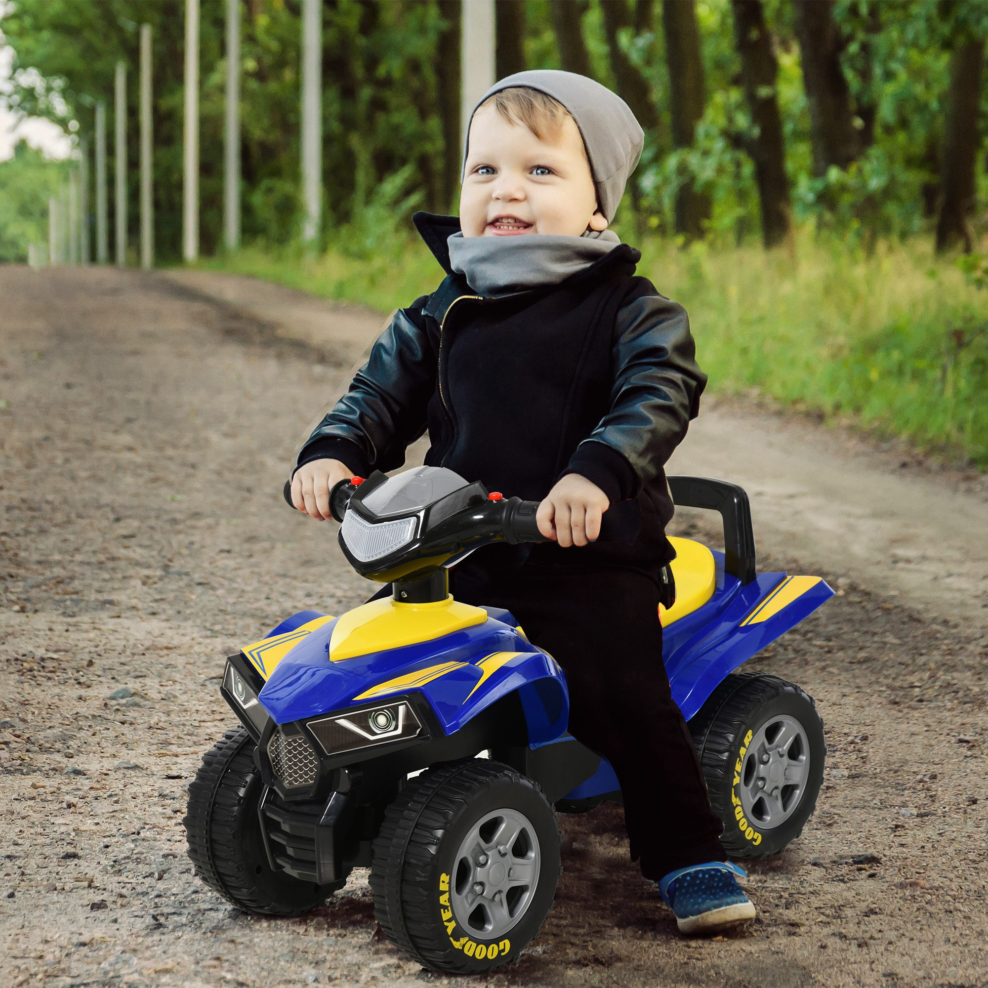 Un bambino con giacca e berretto guida un quad giocattolo blu e giallo su un sentiero.