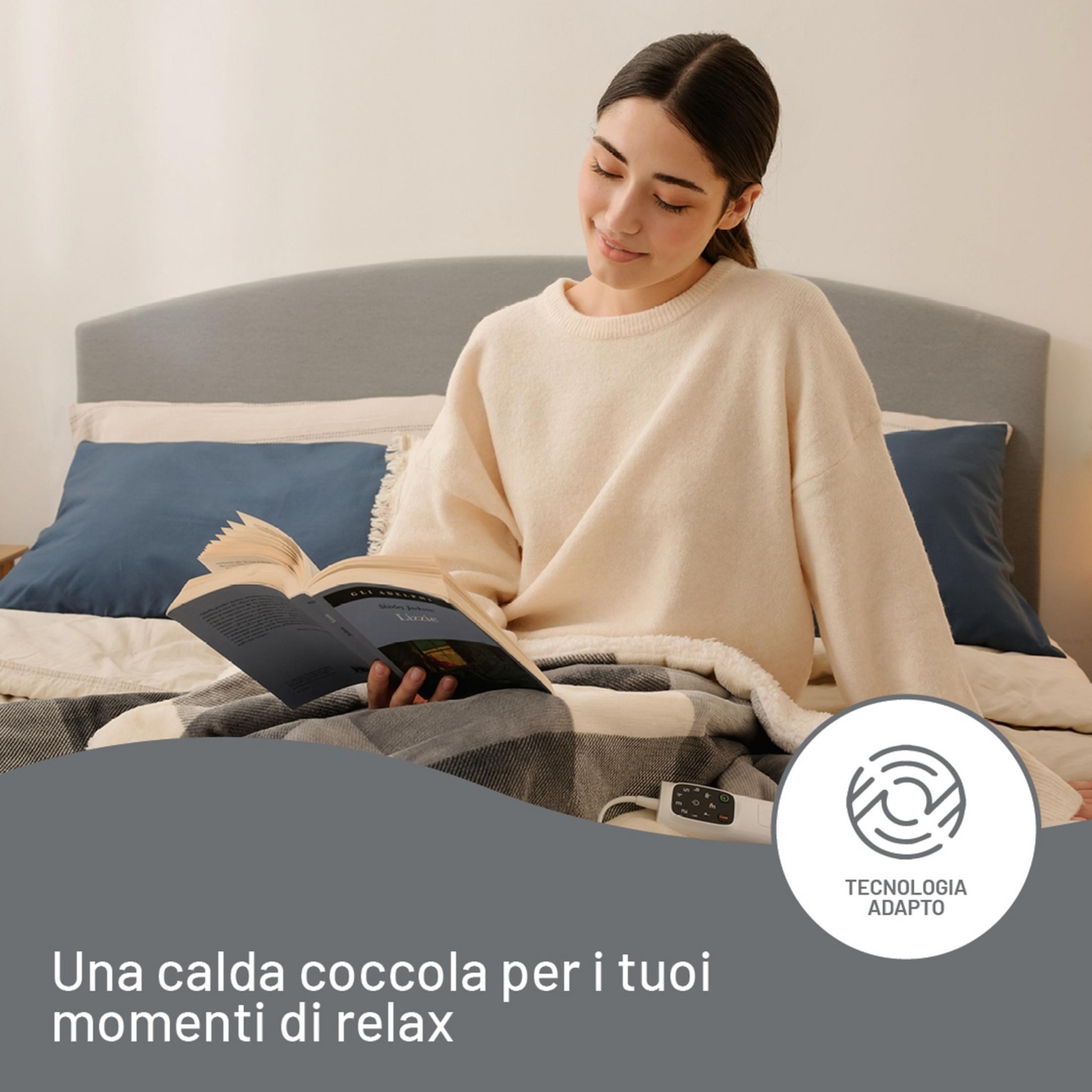 Eine junge Frau liest entspannt ein Buch im Bett, zugedeckt mit einer Decke.