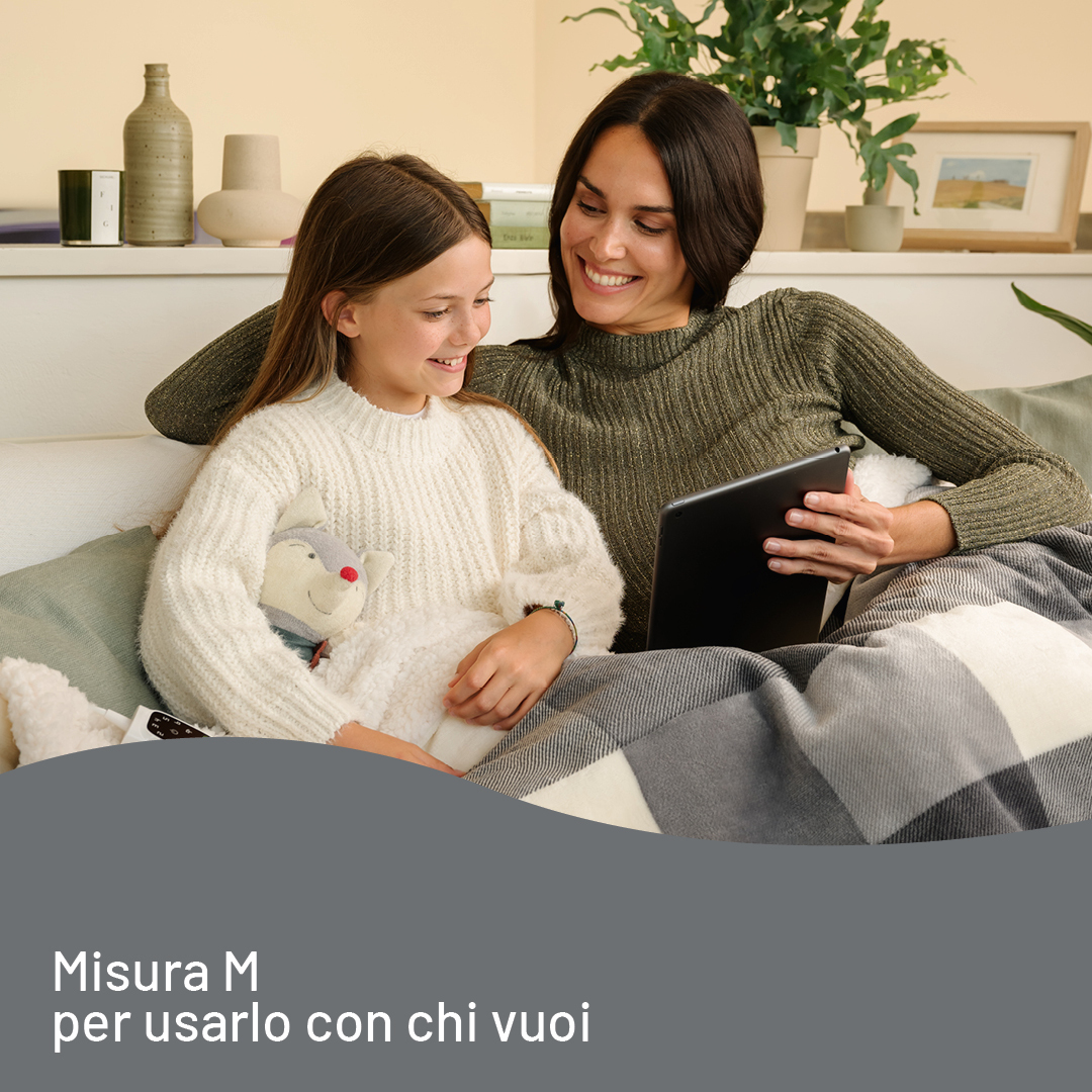 Eine lächelnde Mutter und Tochter sitzen auf einem Sofa und schauen gemeinsam auf ein Tablet.