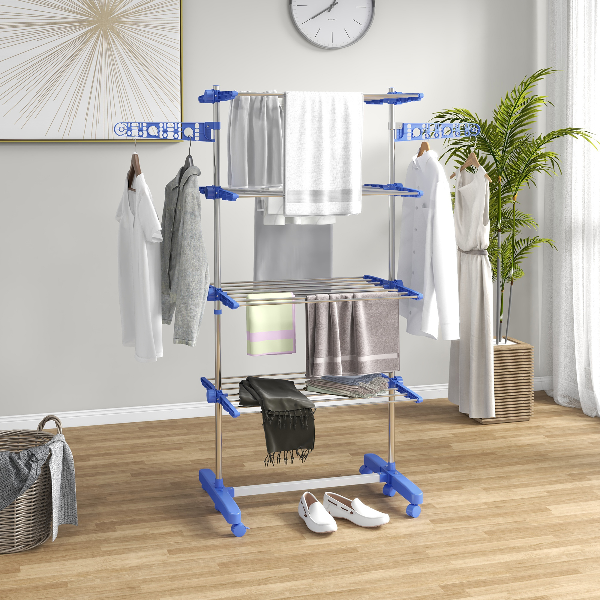 Uno stendibiancheria blu con vestiti si trova su parquet di legno, con piante e quadri sullo sfondo.