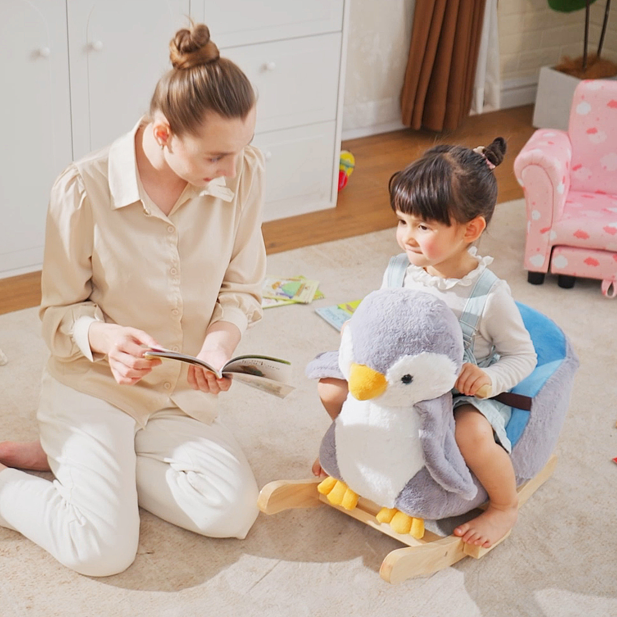Una donna legge un libro a una bambina seduta su un dondolo a forma di pinguino di peluche.