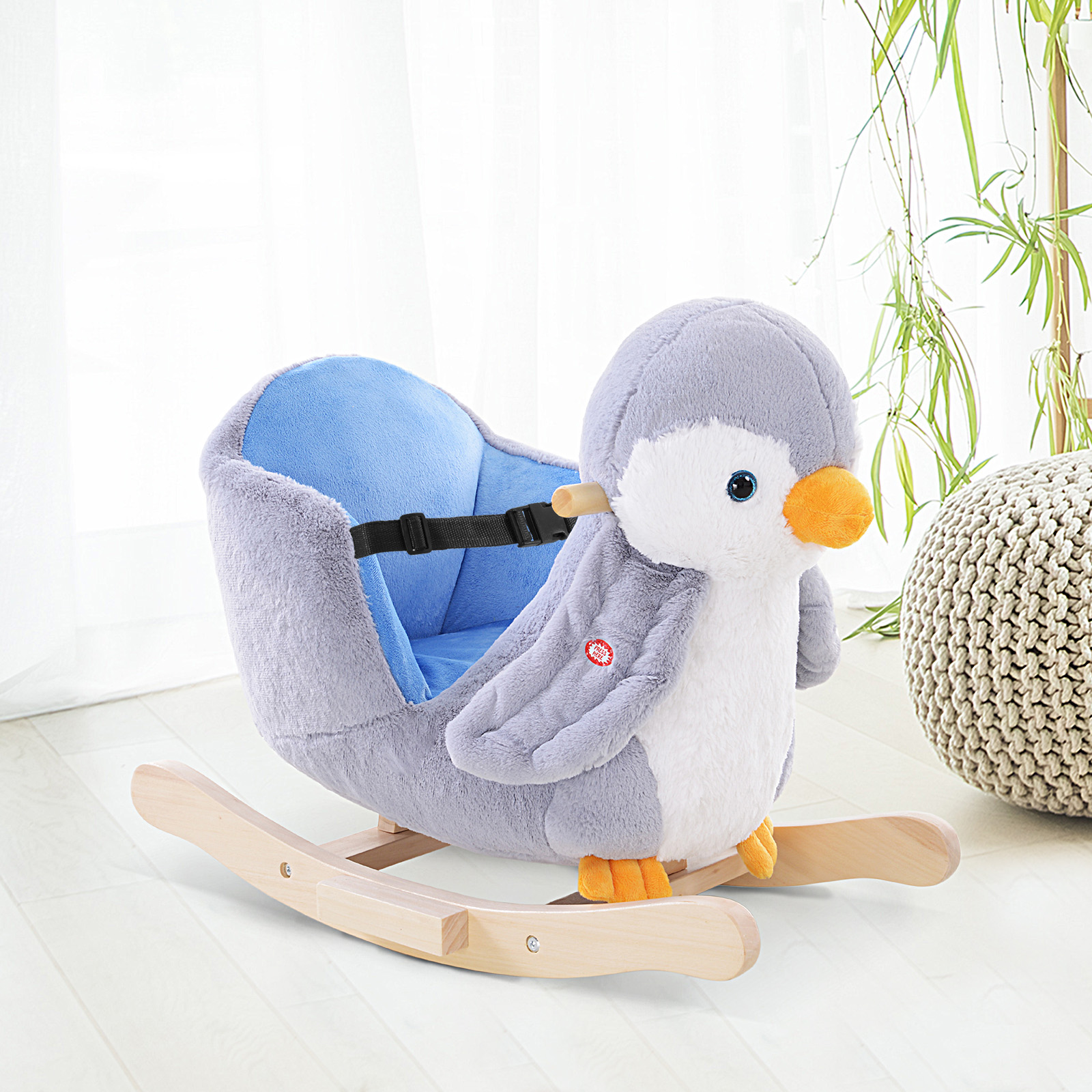 Una sedia a dondolo a forma di pinguino in peluche grigio con seduta blu e pattini di legno in una stanza luminosa.