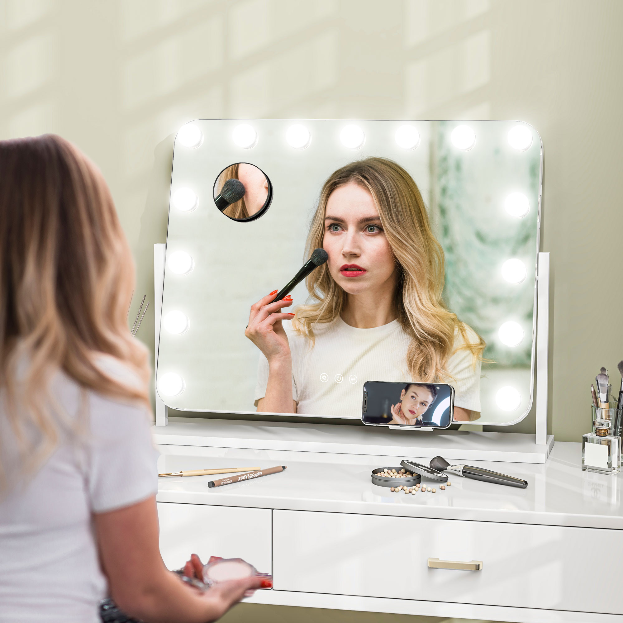 Una donna bionda siede davanti a uno specchio da trucco illuminato e si trucca.