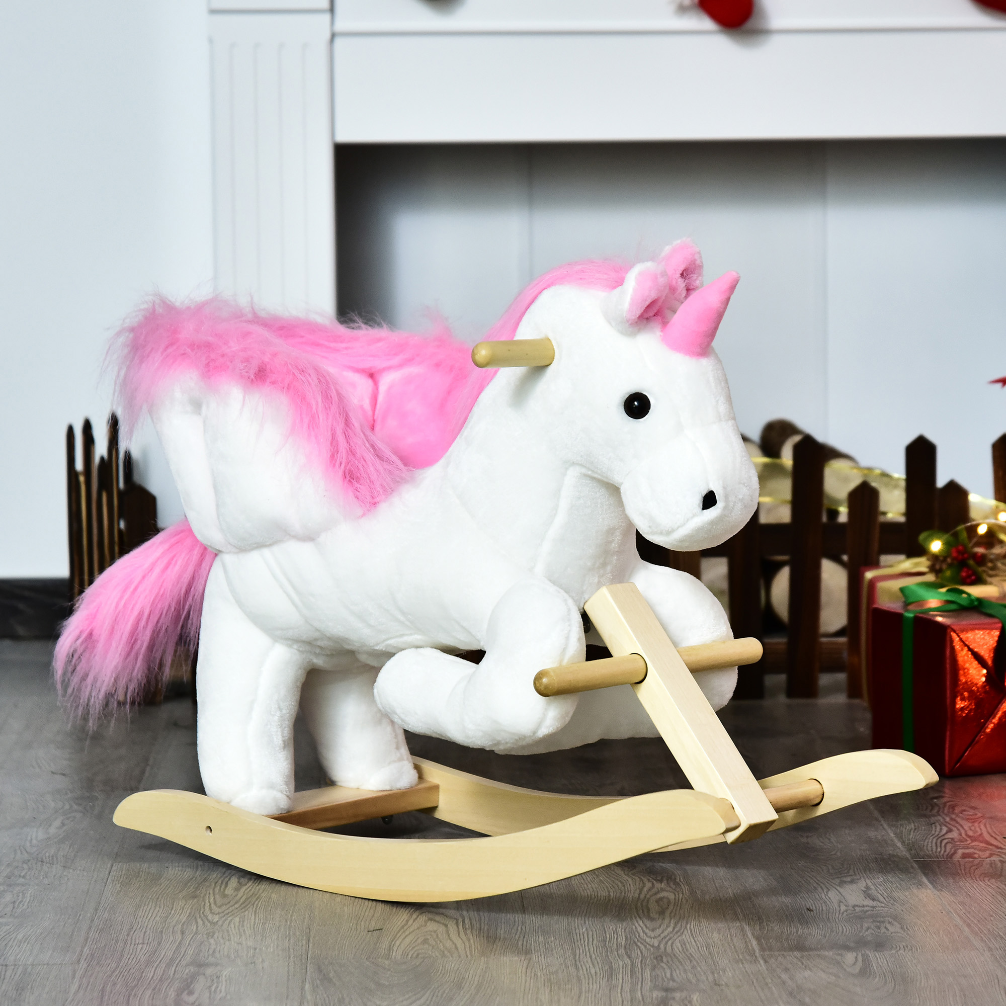 Un unicorno di peluche bianco con criniera rosa e base a dondolo in legno su pavimento in legno davanti a un camino.