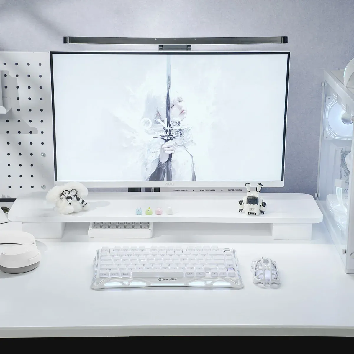 Minimalistyczne białe biurko z monitorem, białą klawiaturą i małymi figurkami w jasnym pokoju.