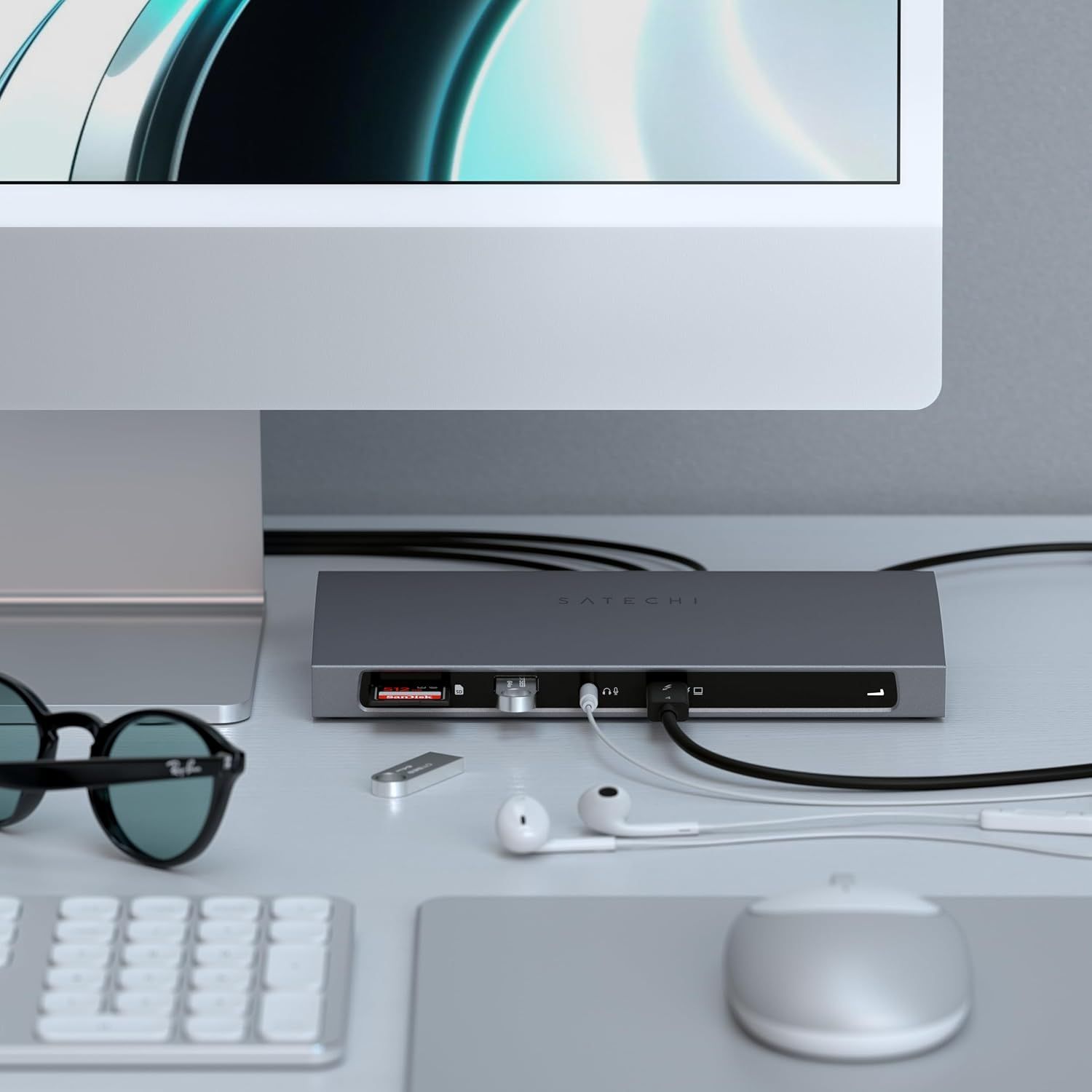 Ein grauer Satechi-Hub mit angeschlossenen Kabeln und SD-Karten auf einem Schreibtisch mit Monitor, Brille und Maus.