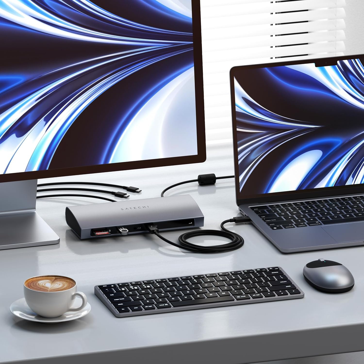 Ein Schreibtisch mit Monitor, Laptop, Satechi-Dock, Tastatur, Maus und Kaffeetasse mit passenden blauen abstrakten Tapeten.