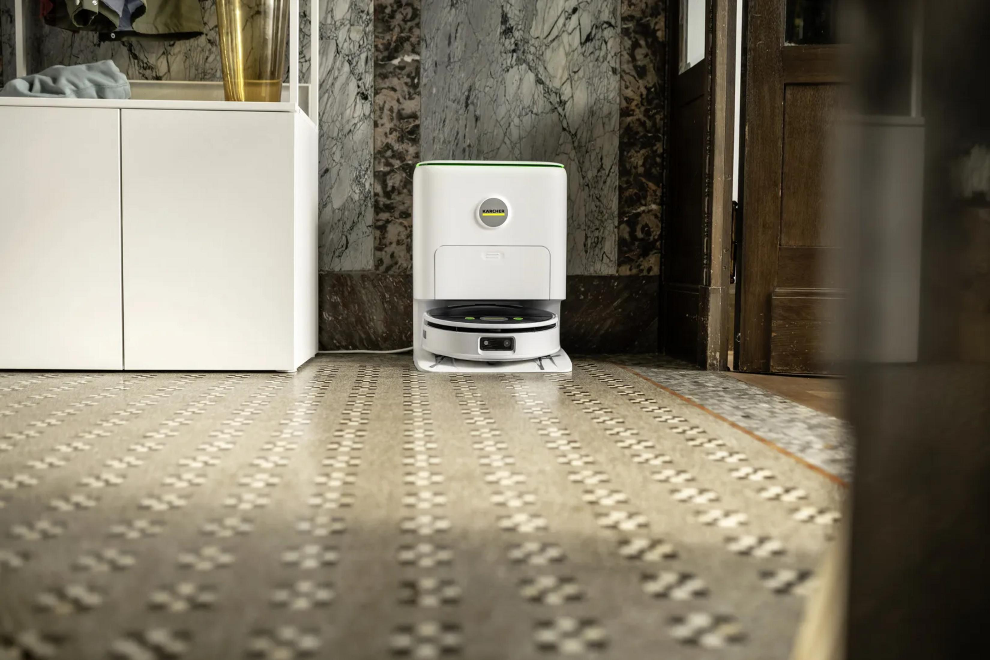 Un robot aspirapolvere bianco nella sua base di ricarica su piastrelle decorate davanti a una parete.