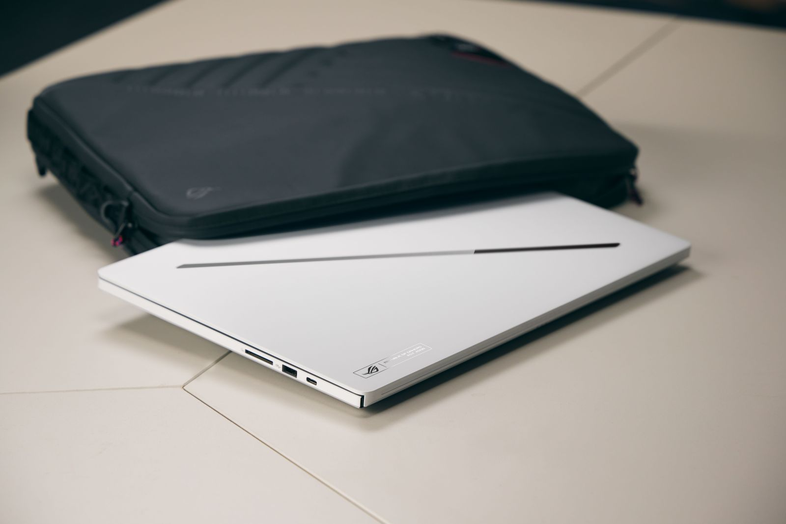 Ein weißer Laptop liegt vor einer schwarzen Laptoptasche auf einem hellen Tisch.